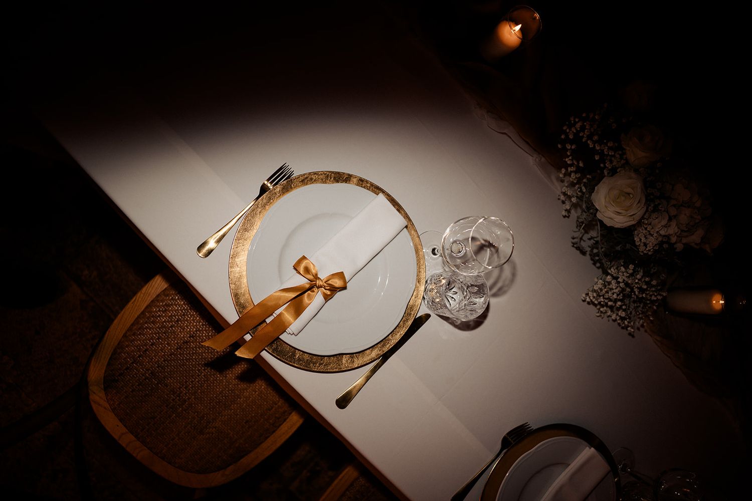 Elegant table setting with gold-rimmed plate, crystal glass, and candle in romantic dim lighting.