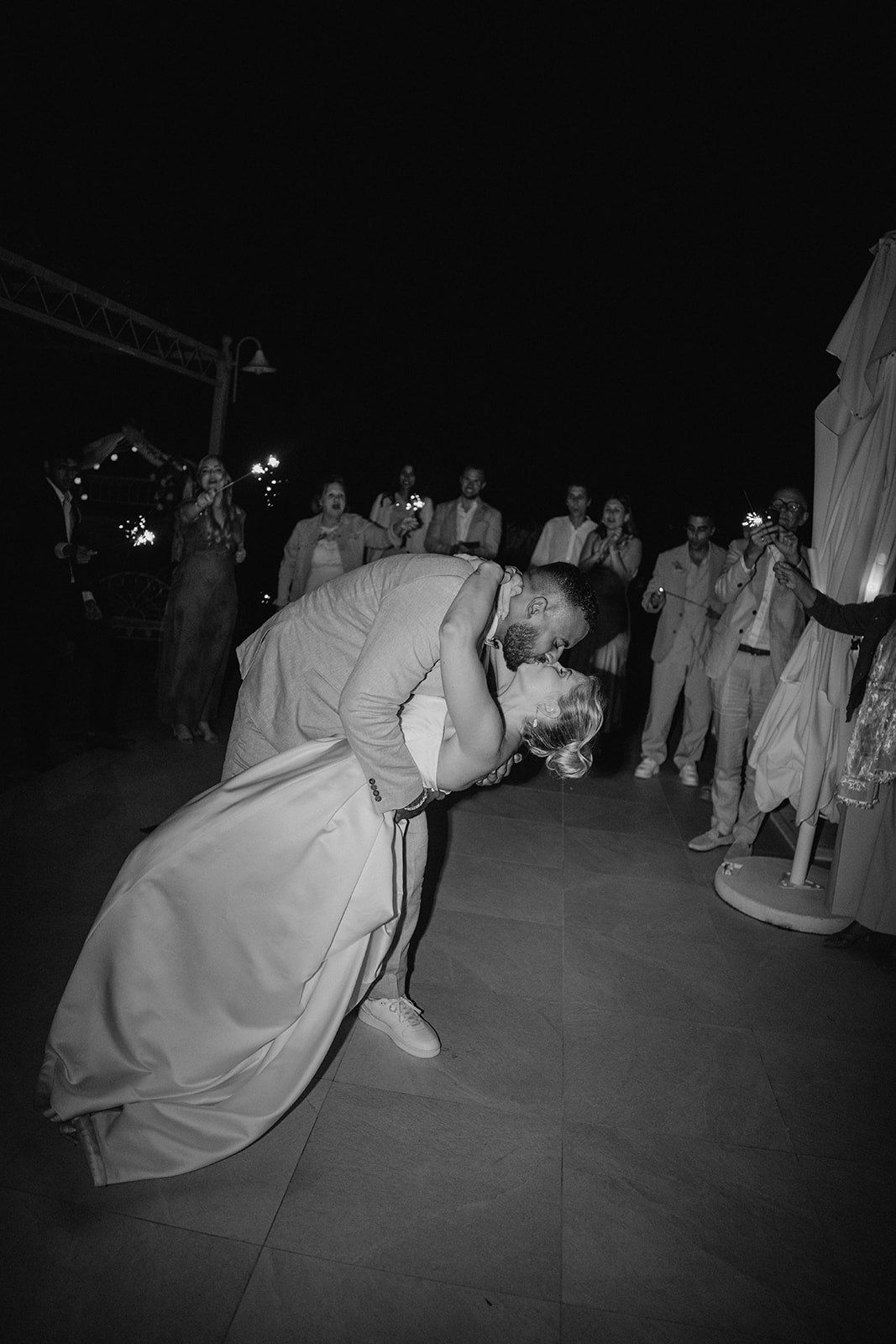 Black and white photo of groom dipping bride for romantic kiss on wedding dance floor.
