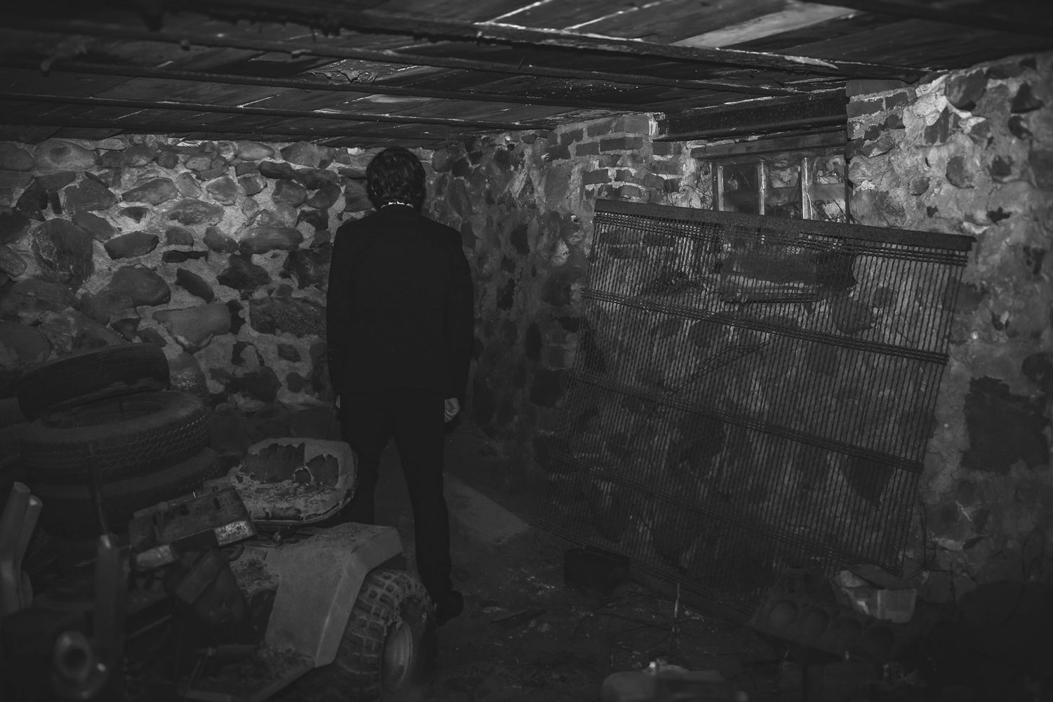 A dark silhouette stands in a dimly lit basement with stone walls and scattered debris on the floor.