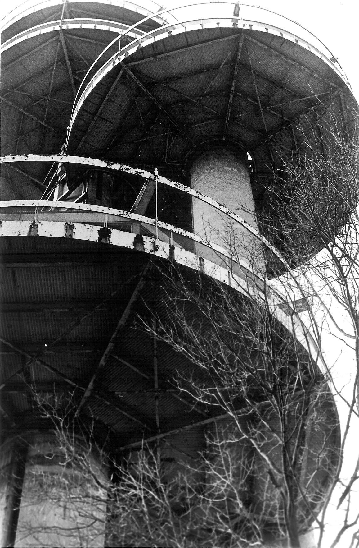 A black and white photograph of a spiral staircase winding around a tall tower with metal railings and curved canopies.