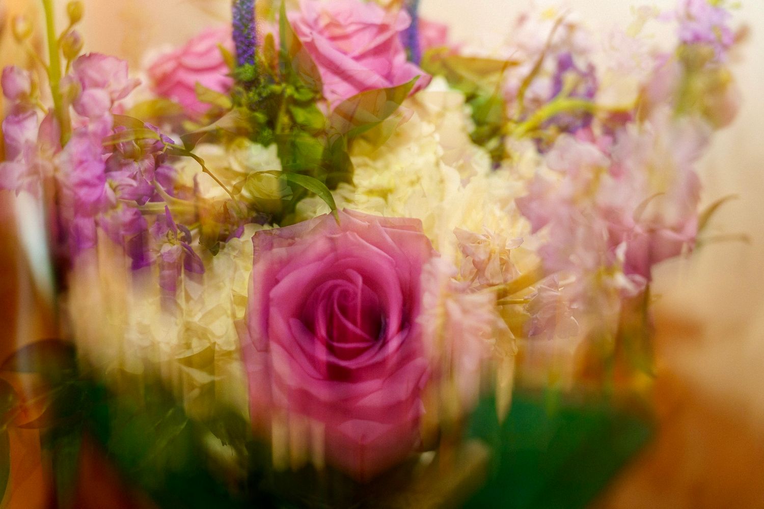 Soft focus bouquet of pink roses, white hydrangeas, and purple flowers in a dreamy, blurred floral arrangement.