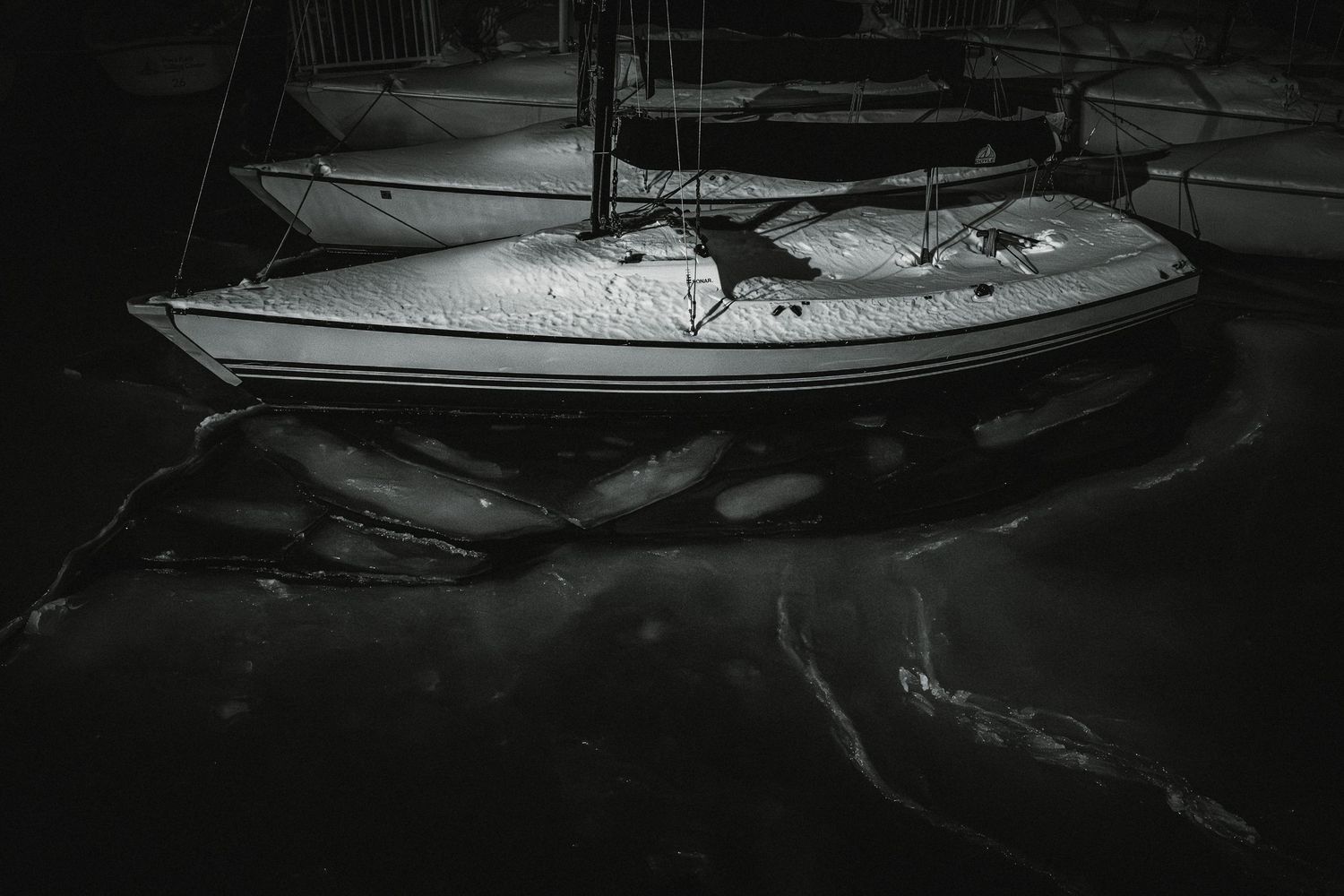 Black and white sailboats moored in a calm marina at night with dramatic lighting and reflections on the water.