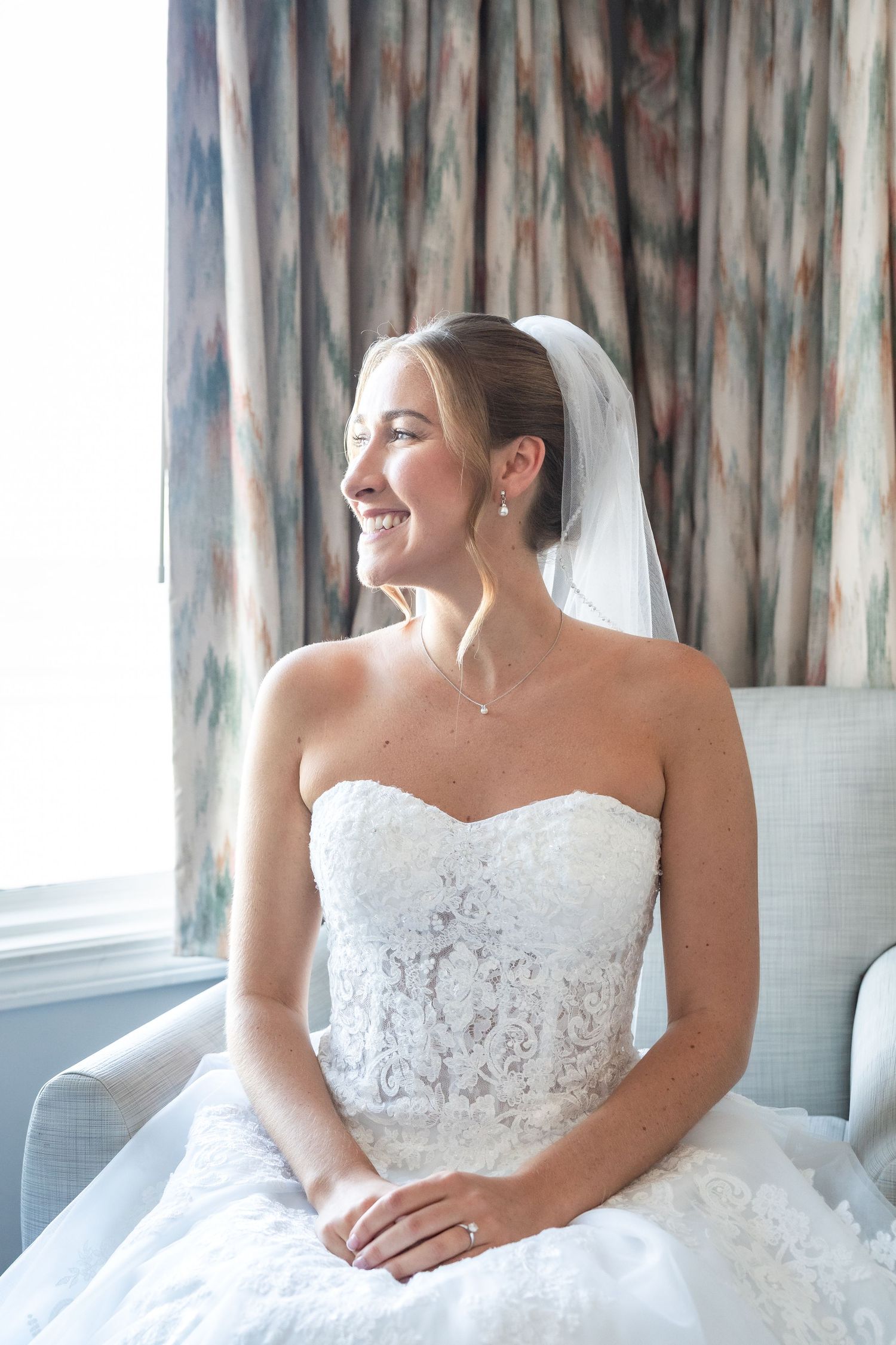 A bride in a white lace strapless wedding gown sits by a window in a series of candid poses.