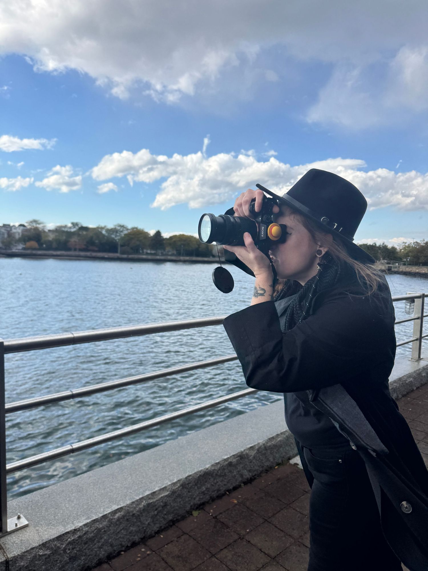 A person using binoculars to observe wildlife while standing on a pier overlooking a lake on a sunny day.