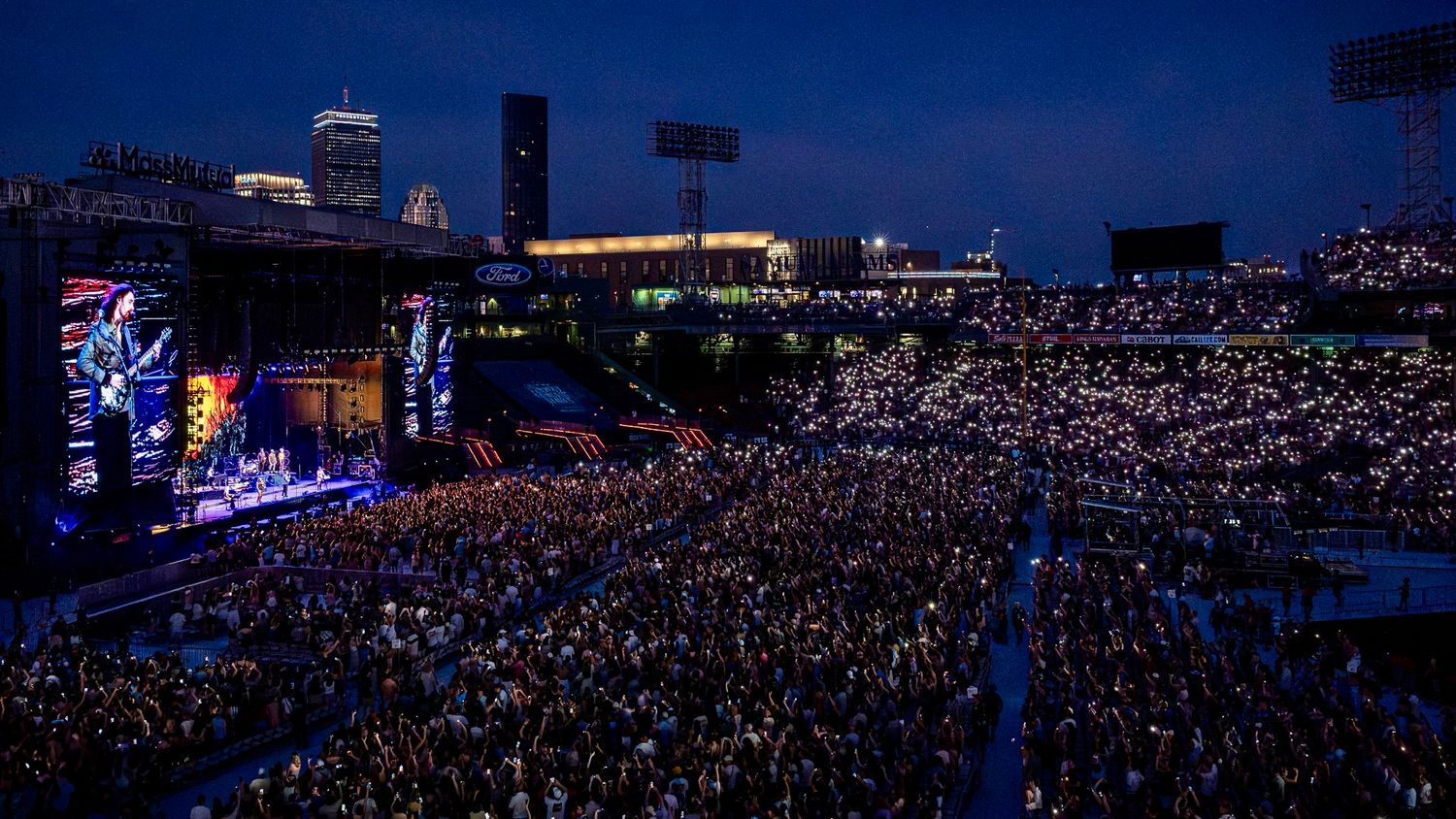 Aerial view of an illuminated concert stadium filled with a massive crowd during a nighttime performance.