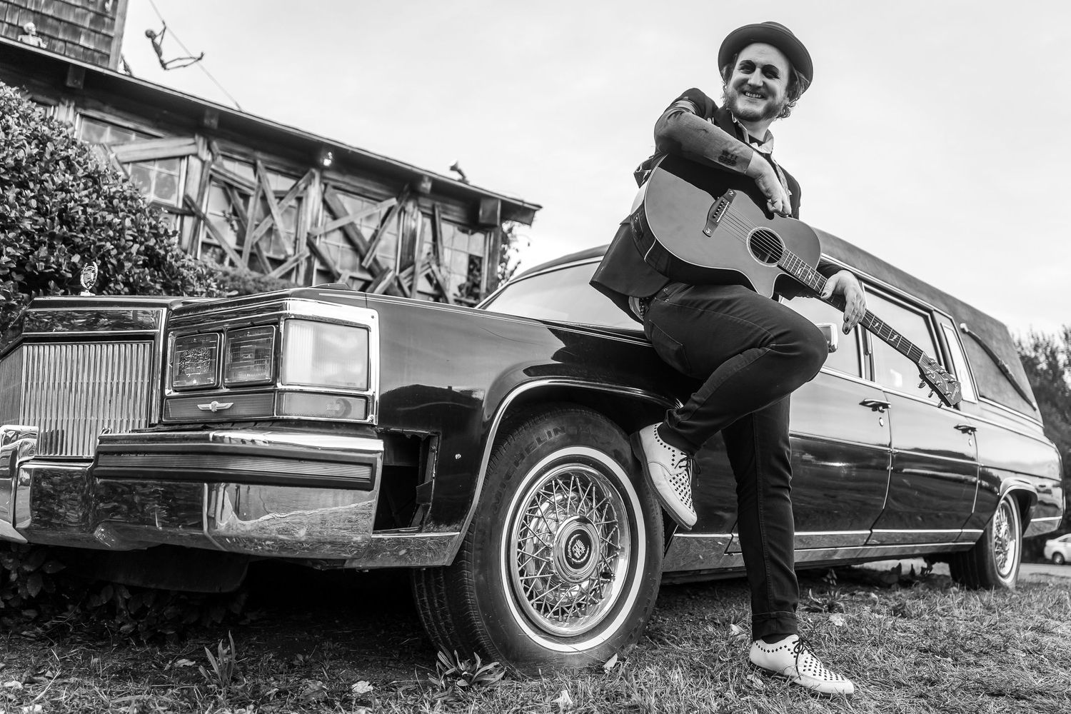 Black and white photo of someone posing on a vintage Cadillac with graffiti in the background.