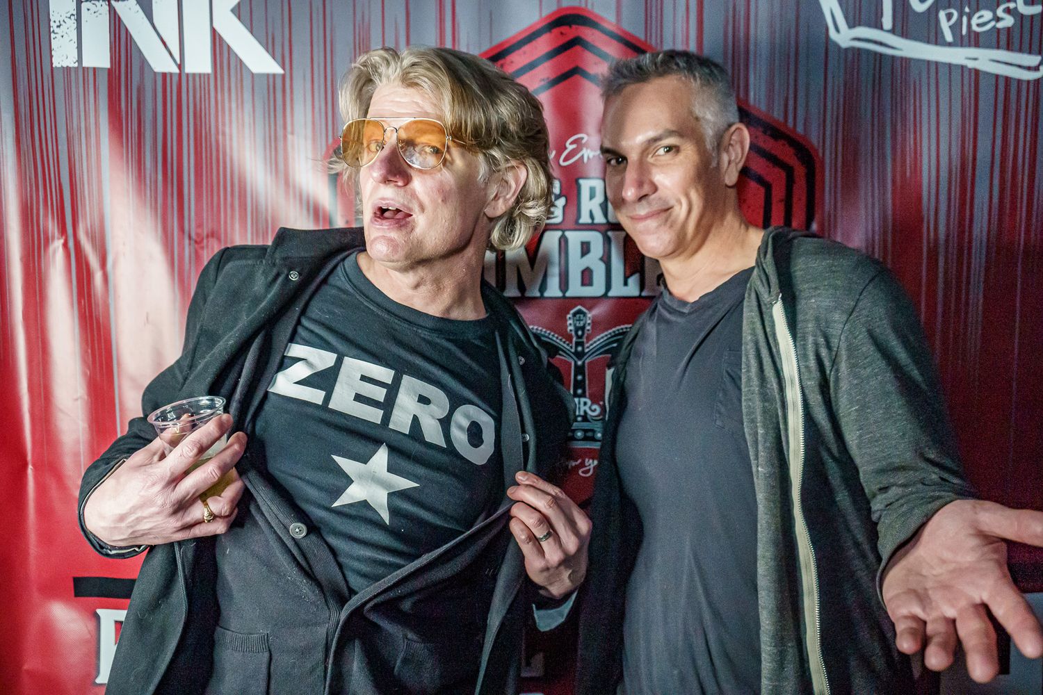 Two people in casual black clothing pose dramatically against a red backdrop with lighting effects.