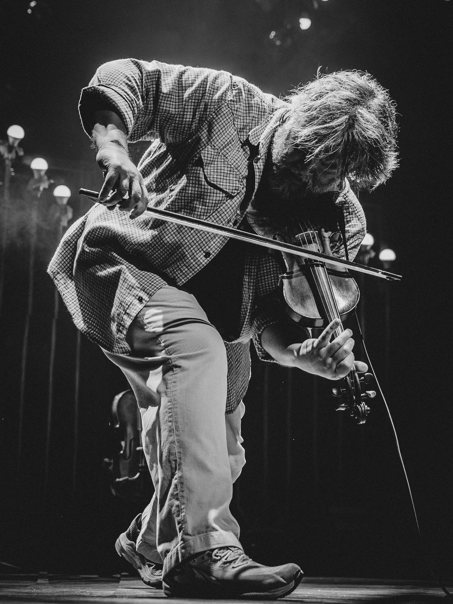 Black and white photo of a male violinist performing on stage, bending dramatically while playing violin.