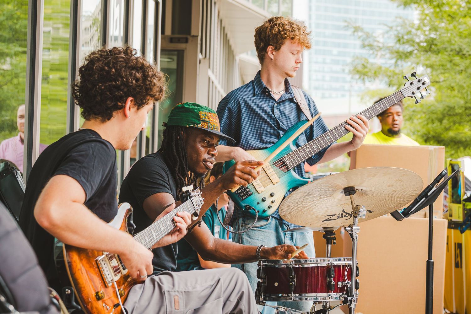 Live band performing outdoors, musicians playing electric guitars and drums on a patio stage in daylight.