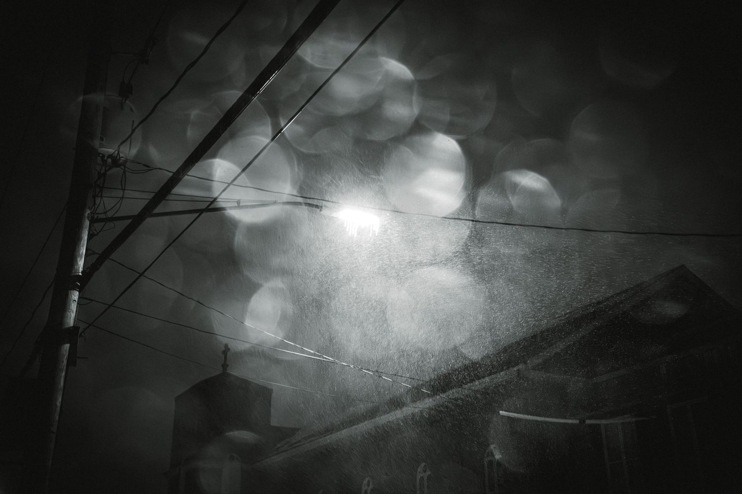 Dark moody cityscape at night with power lines silhouetted against bokeh lights and cloudy sky.
