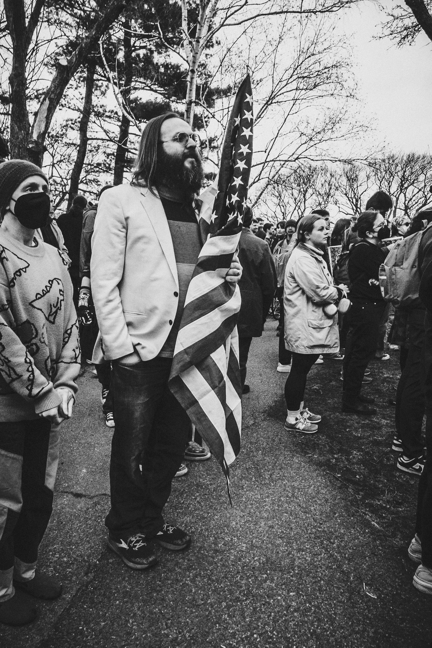 A group of people gathered outdoors in winter, with one person holding an American flag during a protest or rally.