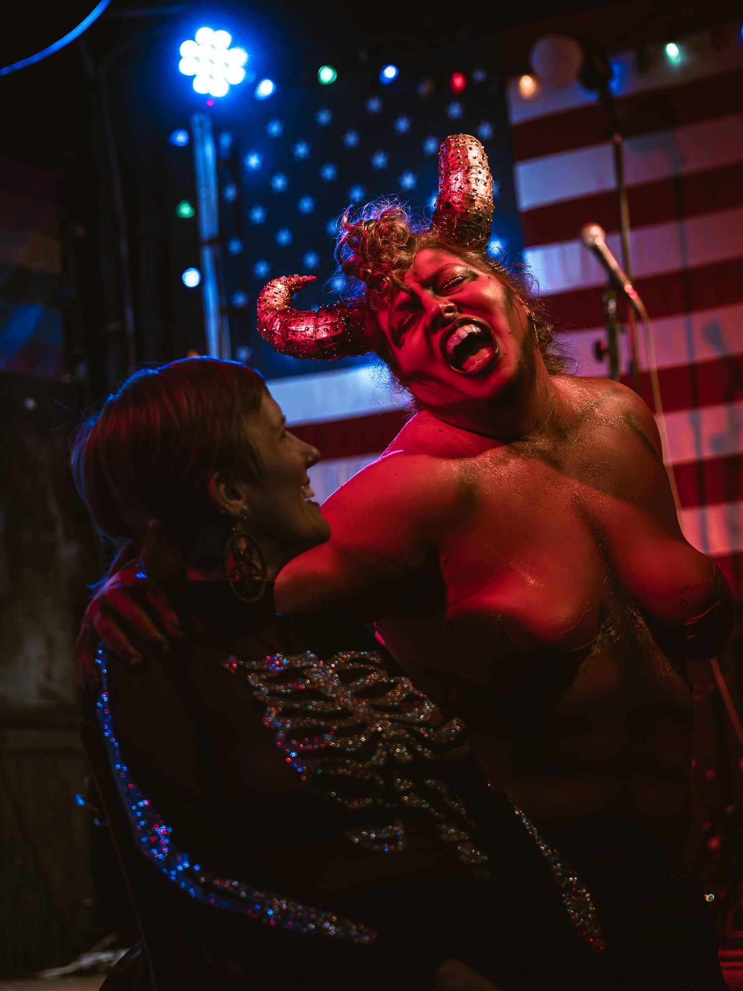 A dimly lit nightclub scene with red and blue lighting creates a moody atmosphere during a performance.