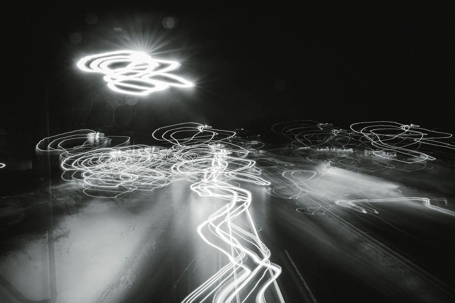Long exposure night photograph showing light trails from traffic creating abstract white streaks against a dark background.