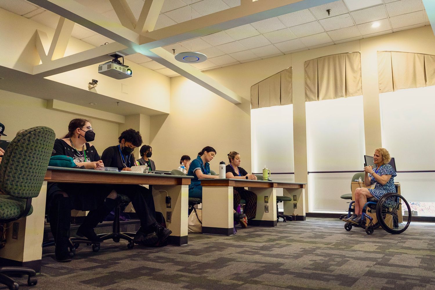 Students attend a lecture in a classroom while a presenter in a wheelchair speaks at the front of the room.