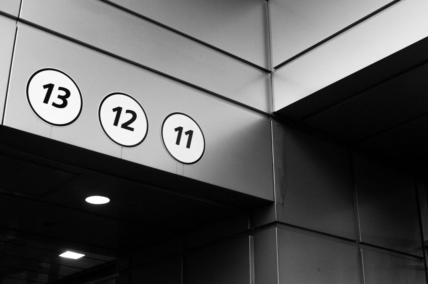 Black and white view of elevator floor numbers 13, 12, and 11 mounted on a wall with modern lighting fixtures.