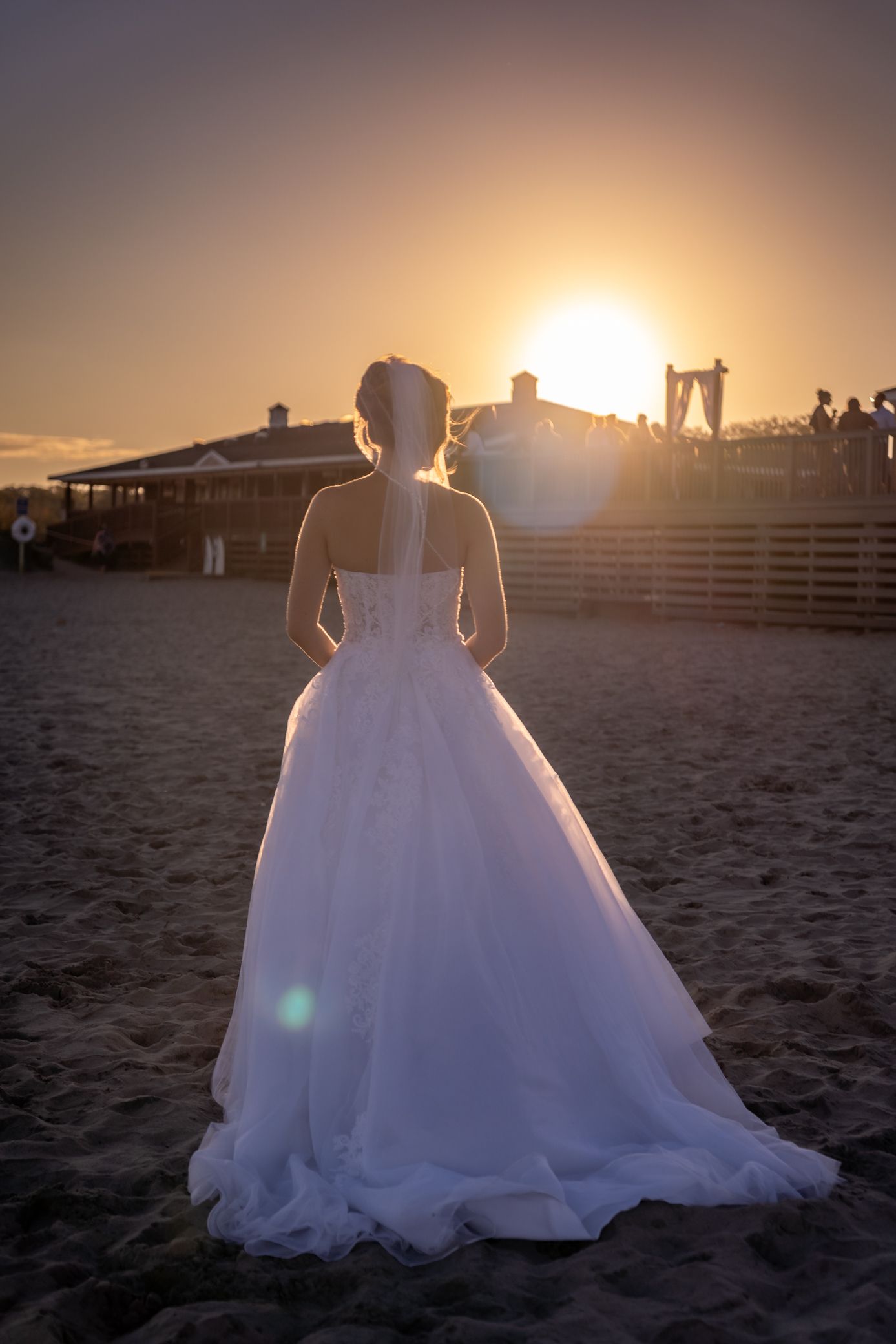 A white wedding gown silhouetted against a dramatic sunset on a sandy beach.