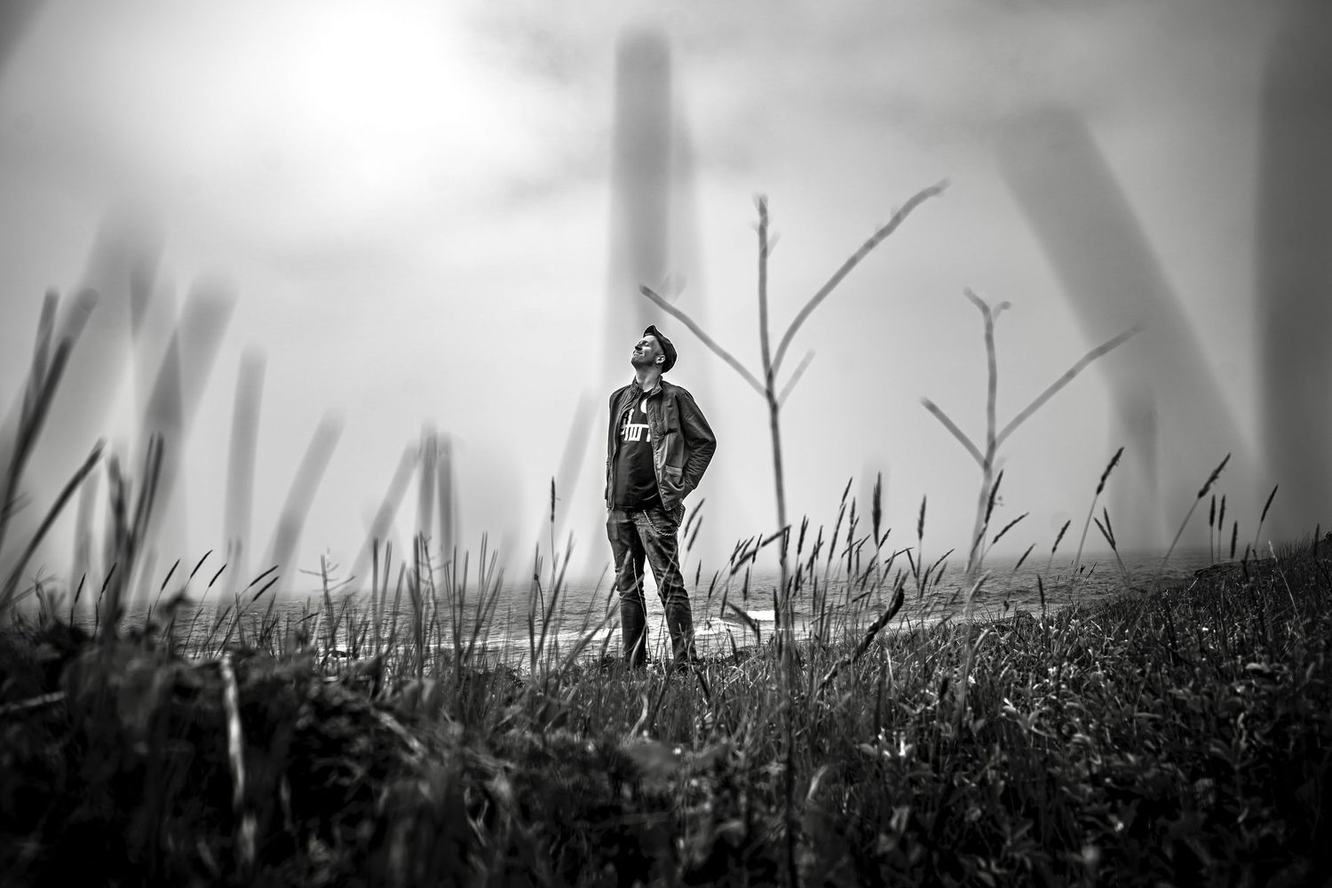 A silhouetted figure stands in a grassy field against a dramatic sky in black and white photography.