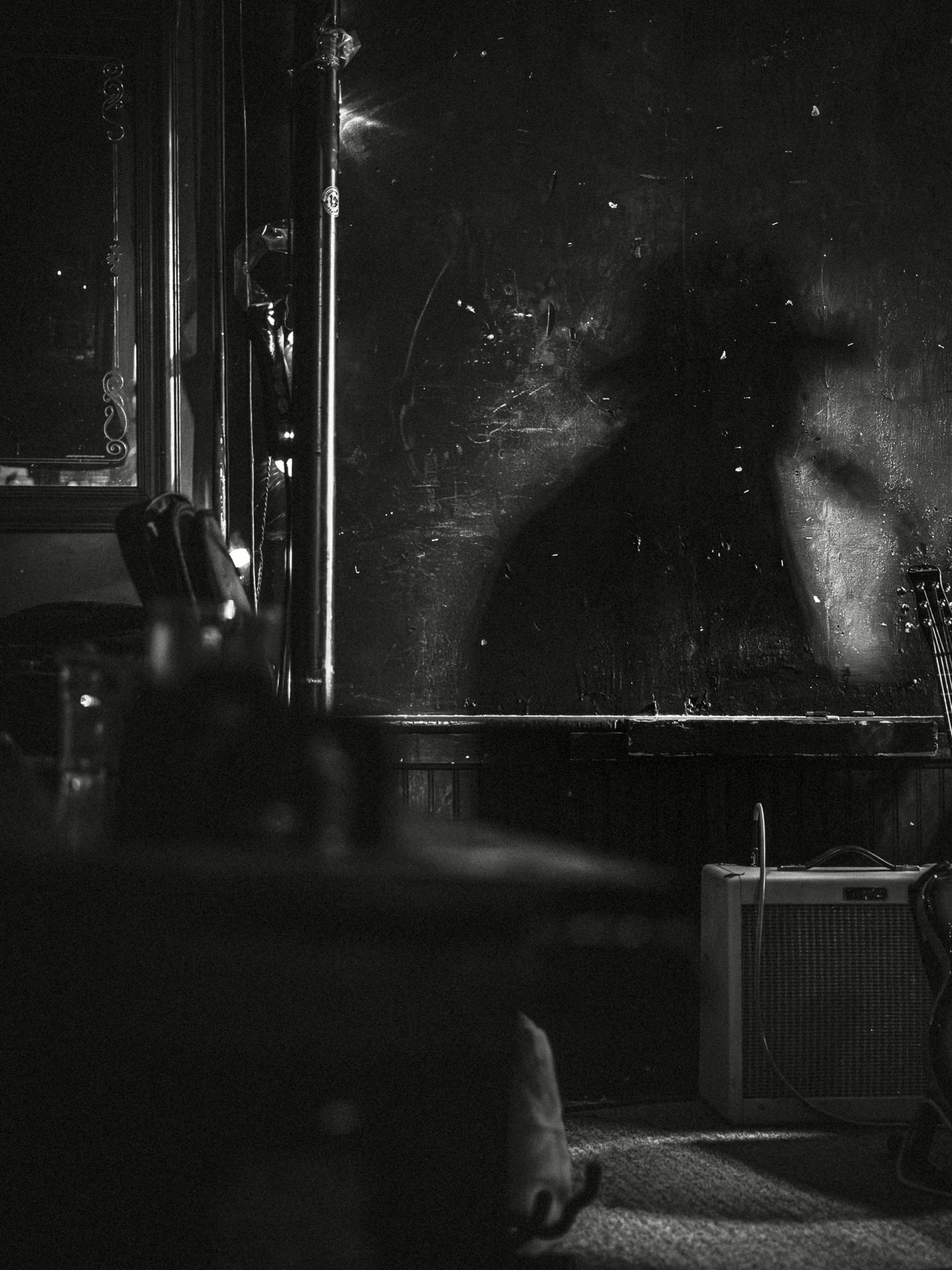 Eerie black and white photo of a shadowy figure reflected in a dark, weathered wall inside a dimly lit room.