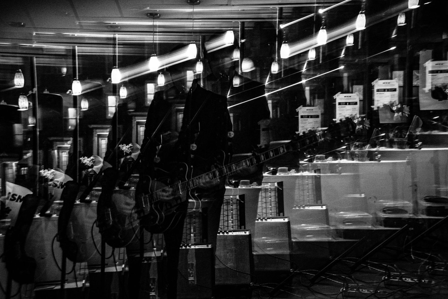 Row of guitars displayed in a dimly lit store, creating a dramatic reflection pattern.