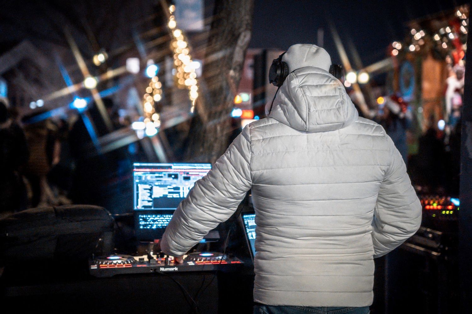 DJ performing at night wearing a white puffy jacket at an outdoor event.