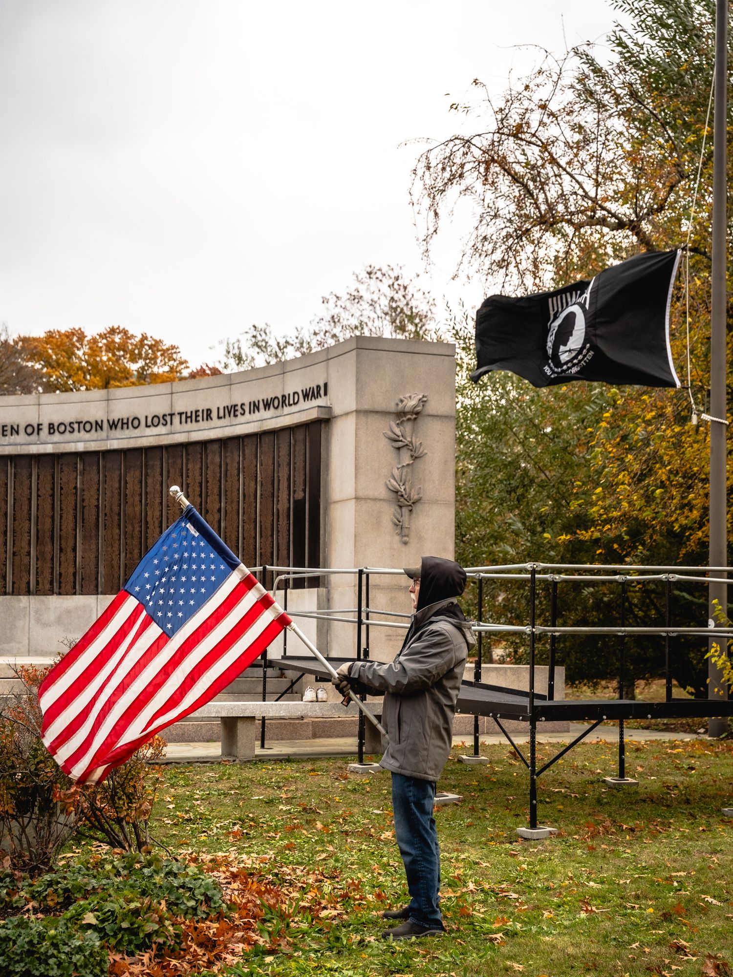 A person places American flags at a memorial site during an autumn day with fallen leaves on the ground.