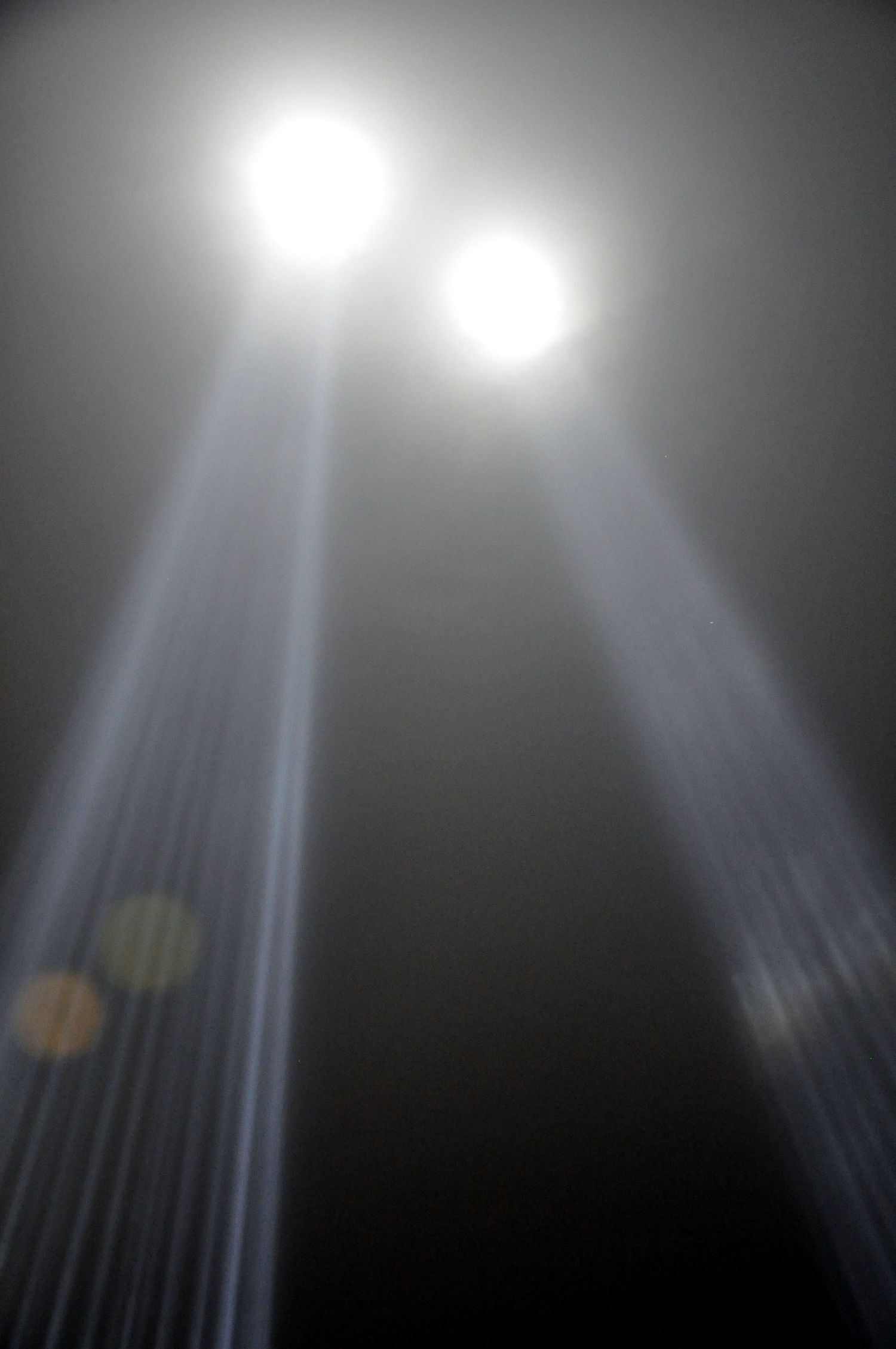 Ethereal light beams pierce through darkness with two bright glowing orbs at the top and lens flare effects.