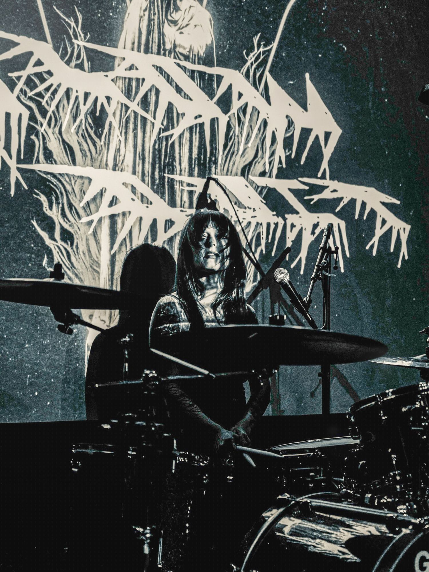 Drummer performing on stage with a dramatic array of white geometric light beams illuminating the dark background.