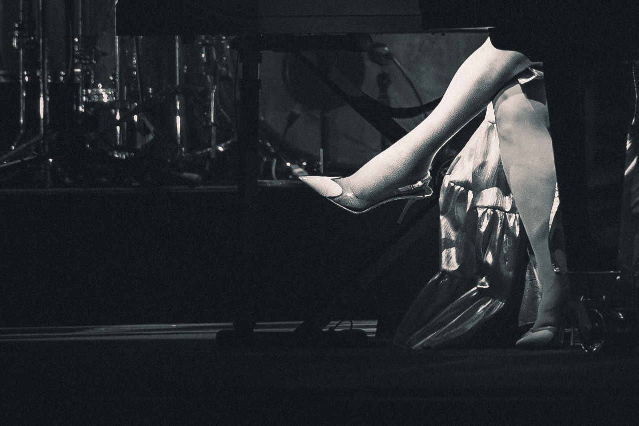 Black and white photo of a performer in a flowing dark gown on stage with musical instruments in background.