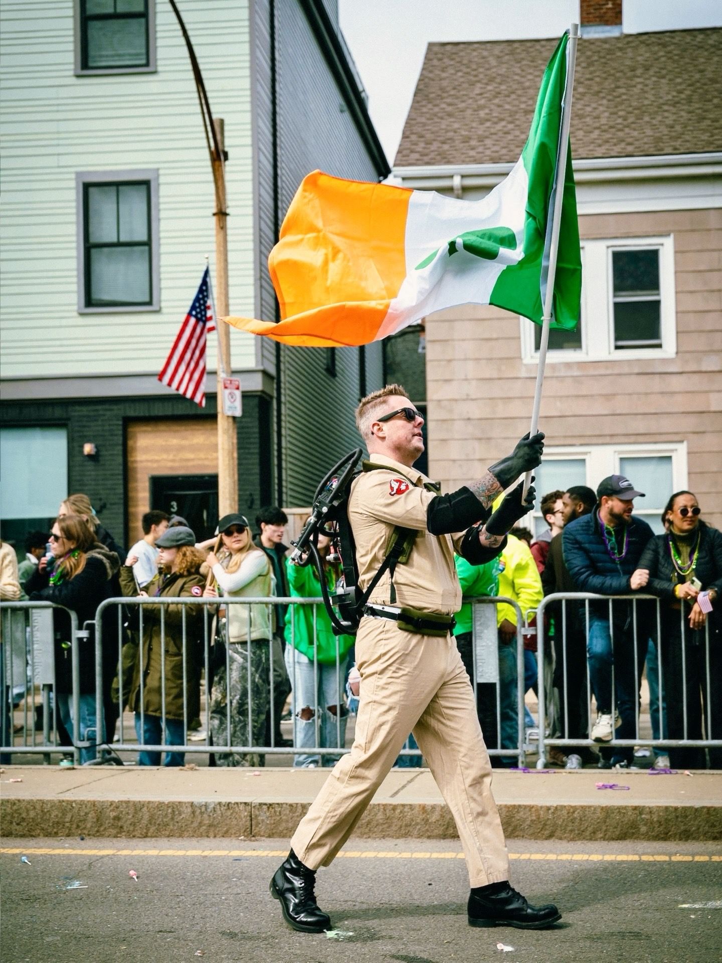A sequence of five photos showing someone marching in beige clothing while holding Irish and American flags during a parade.