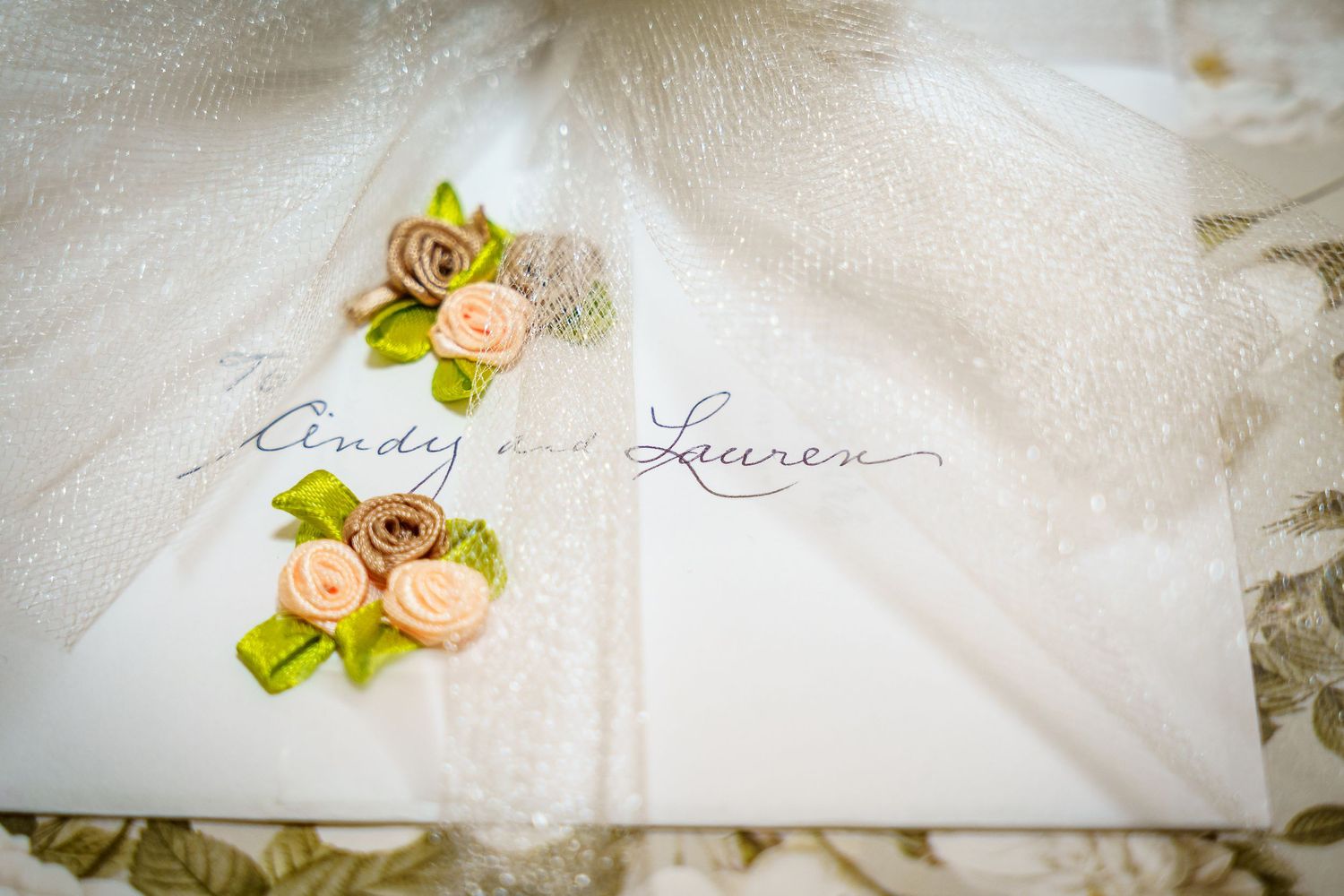 Wedding invitation card with delicate pink floral decorations on white fabric.