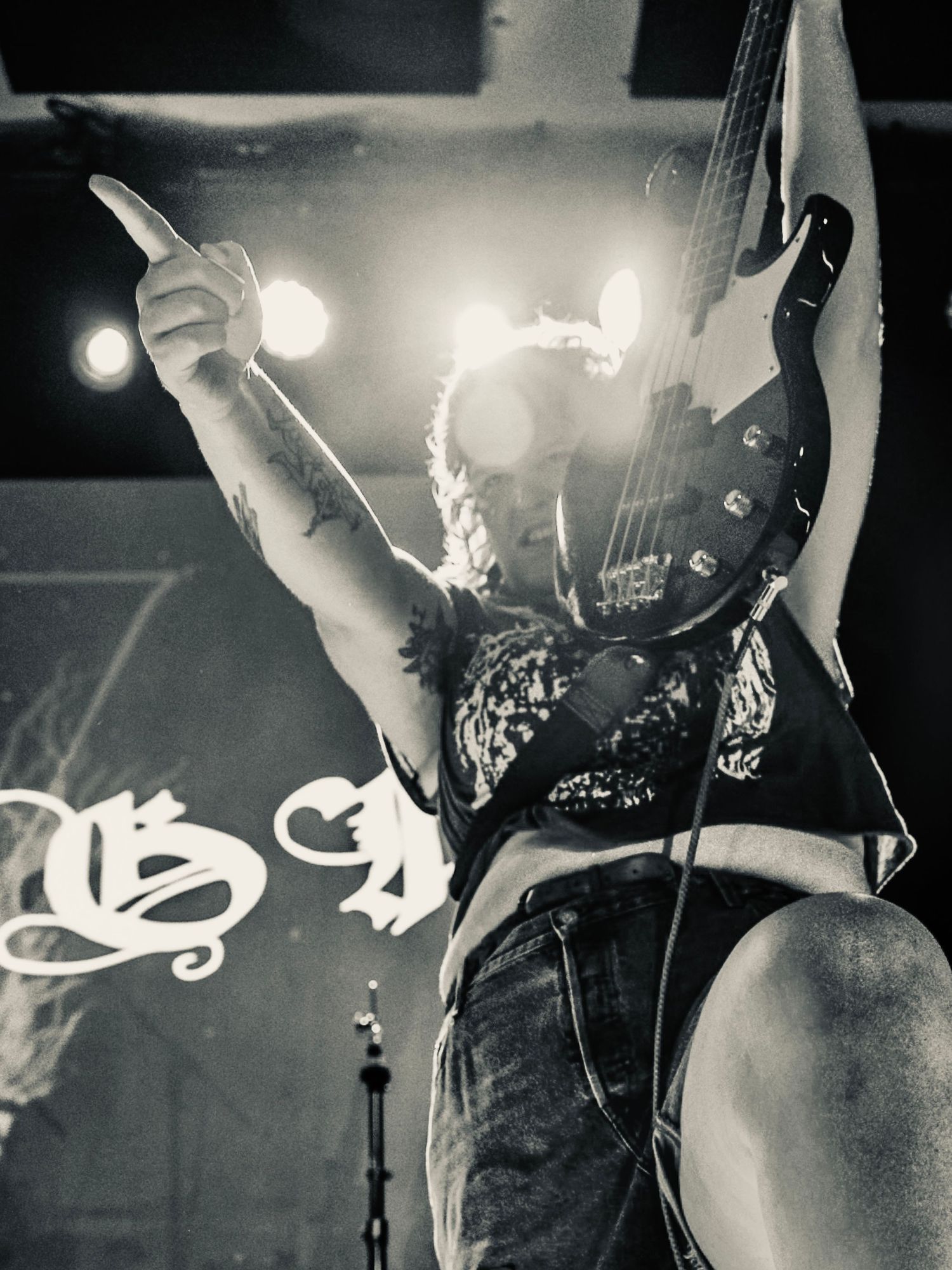 Black and white photo of a rocker performing on stage with hands raised and guitar, shot from a low angle during a concert.