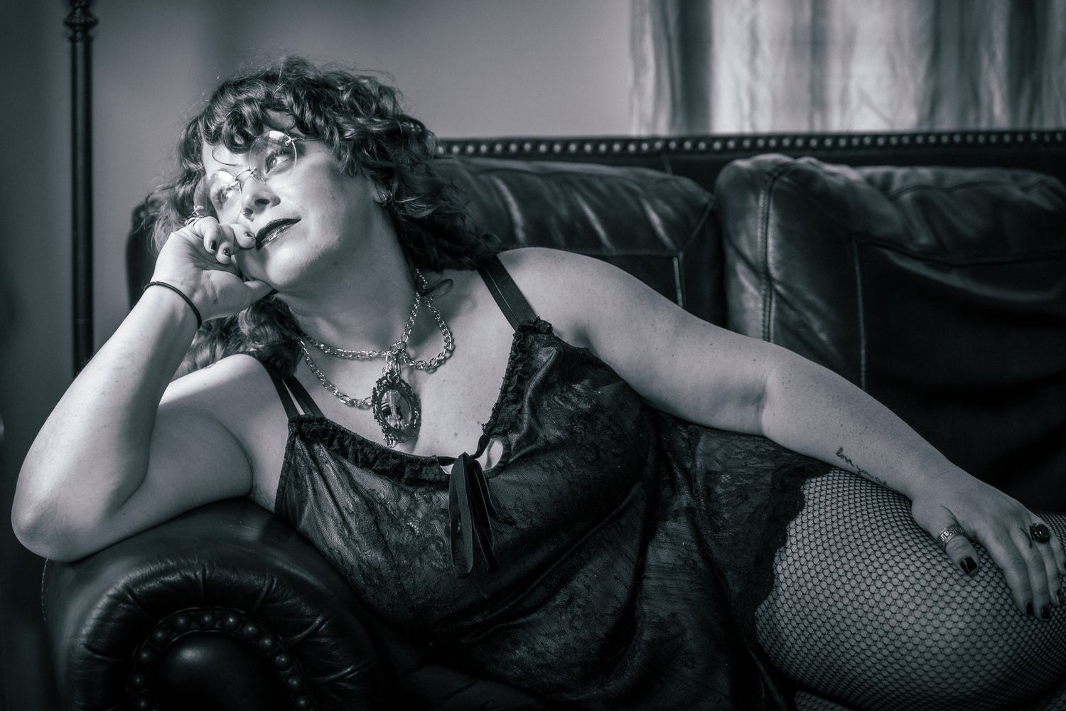 A dramatic black and white boudoir photo of someone in lace lounging on a vintage leather couch.