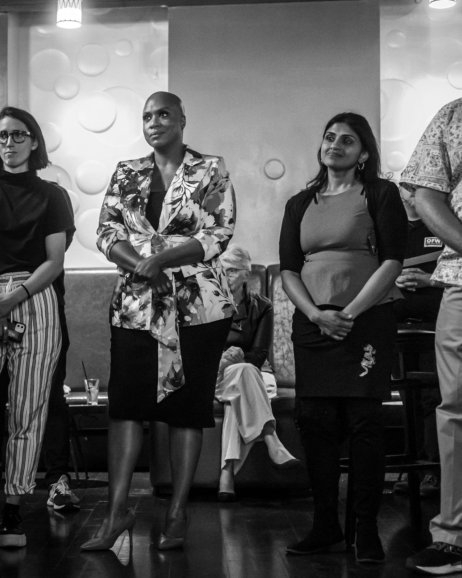 A black and white photo showing people standing together in a group during an indoor event.