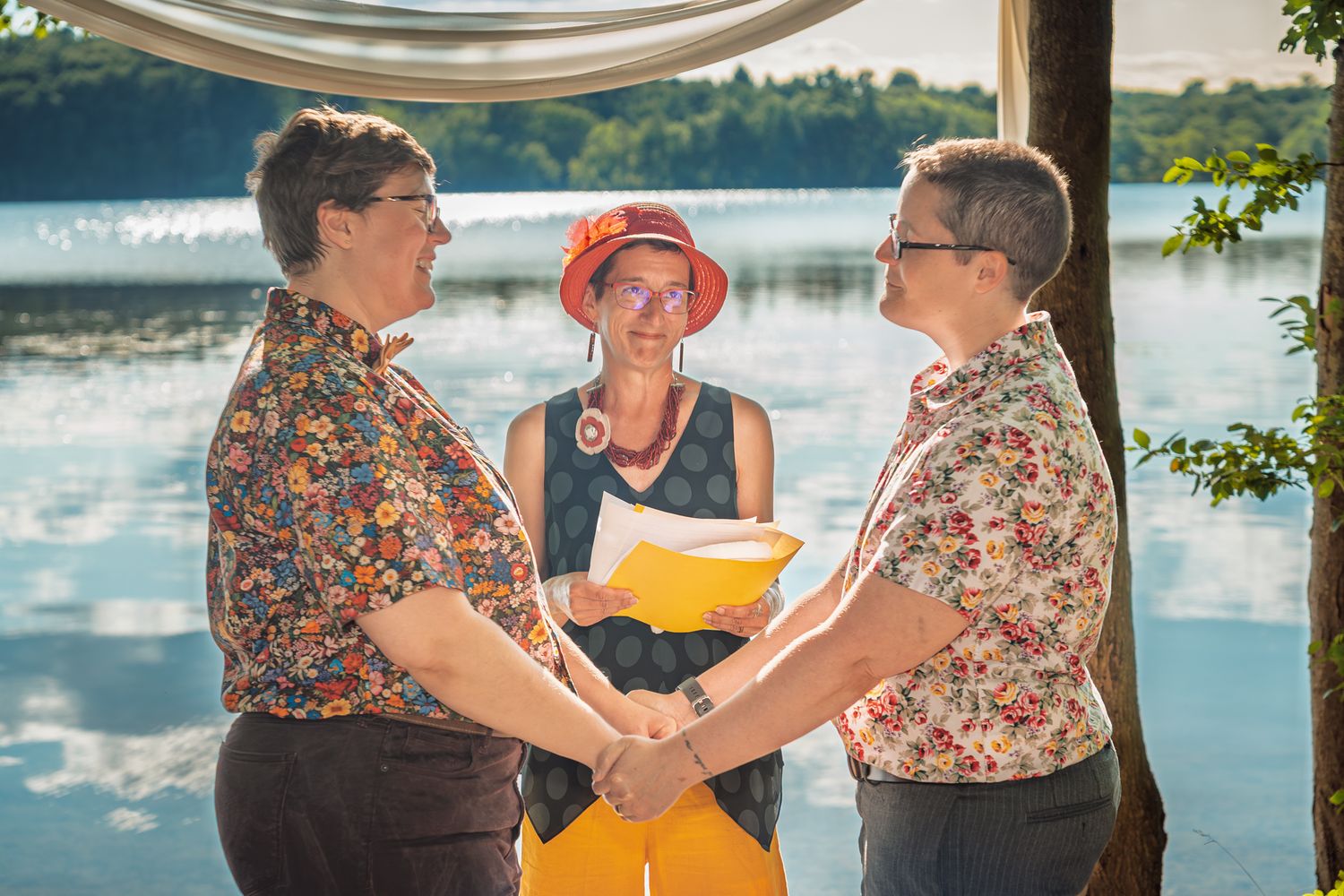 Two people in floral shirts dance together by a scenic lake on a sunny summer afternoon.