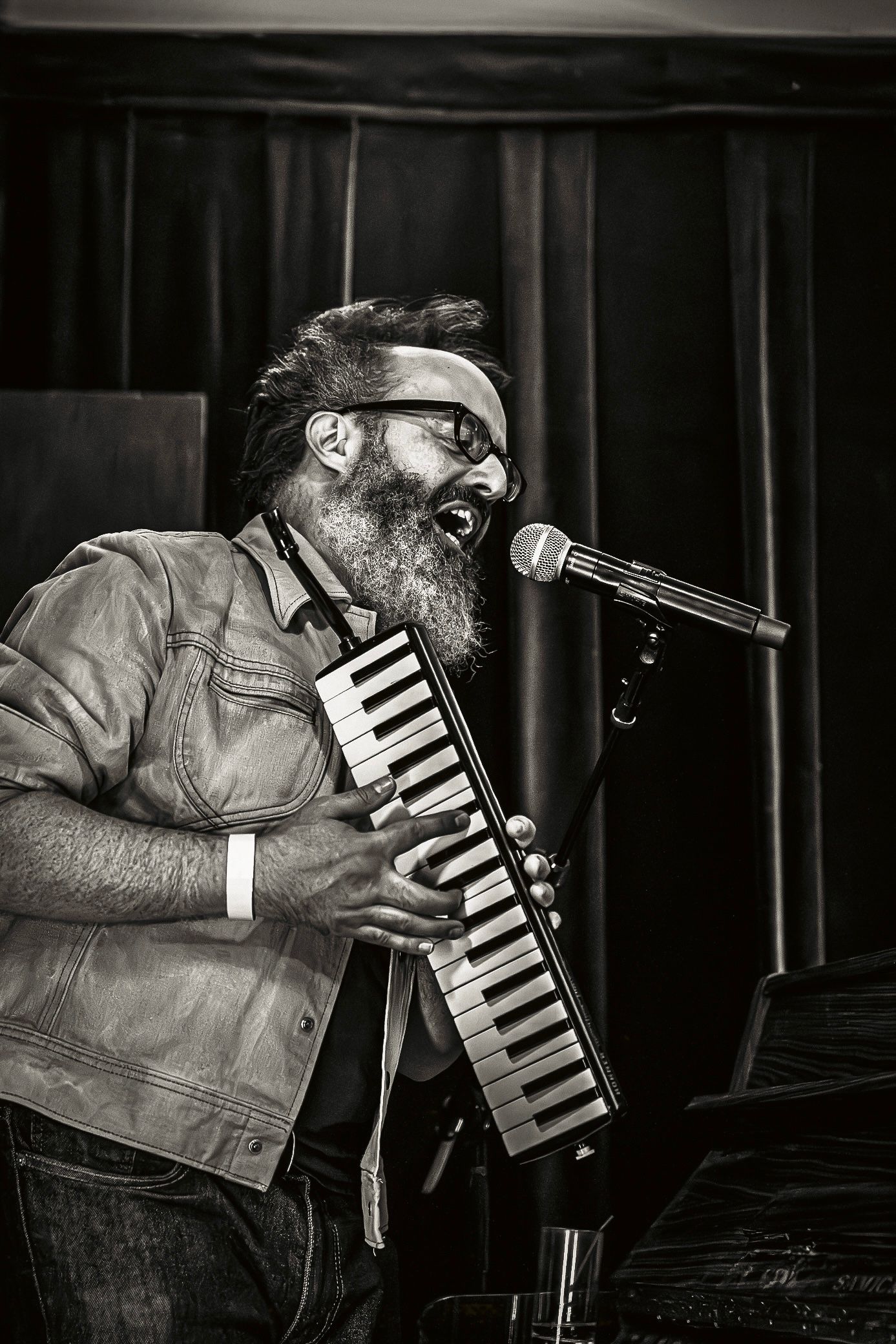 A musician performs on stage with a melodica keyboard instrument at a dimly lit venue.