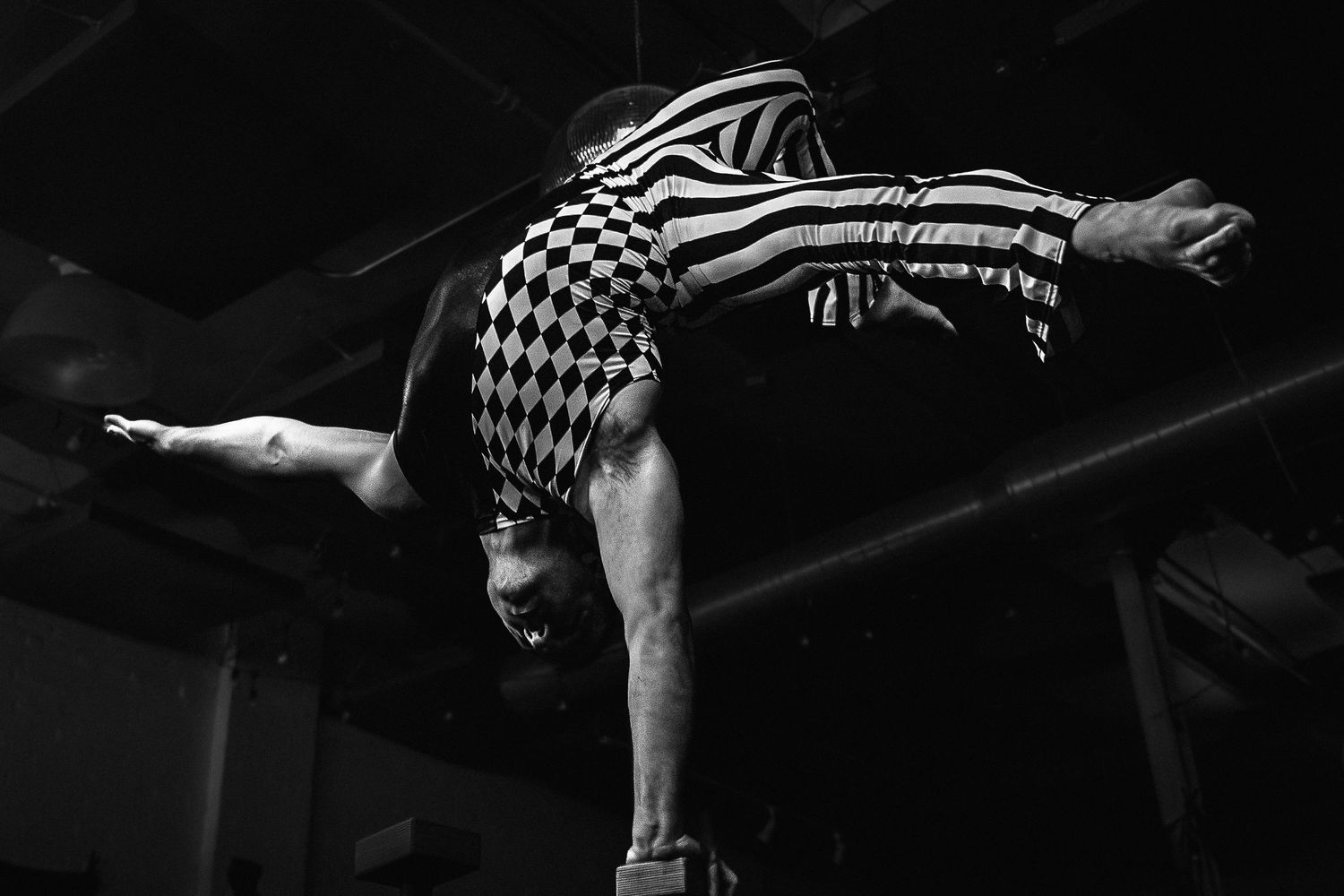 Black and white photo of a gymnast in checkered outfit performing a horizontal balance on parallel bars.