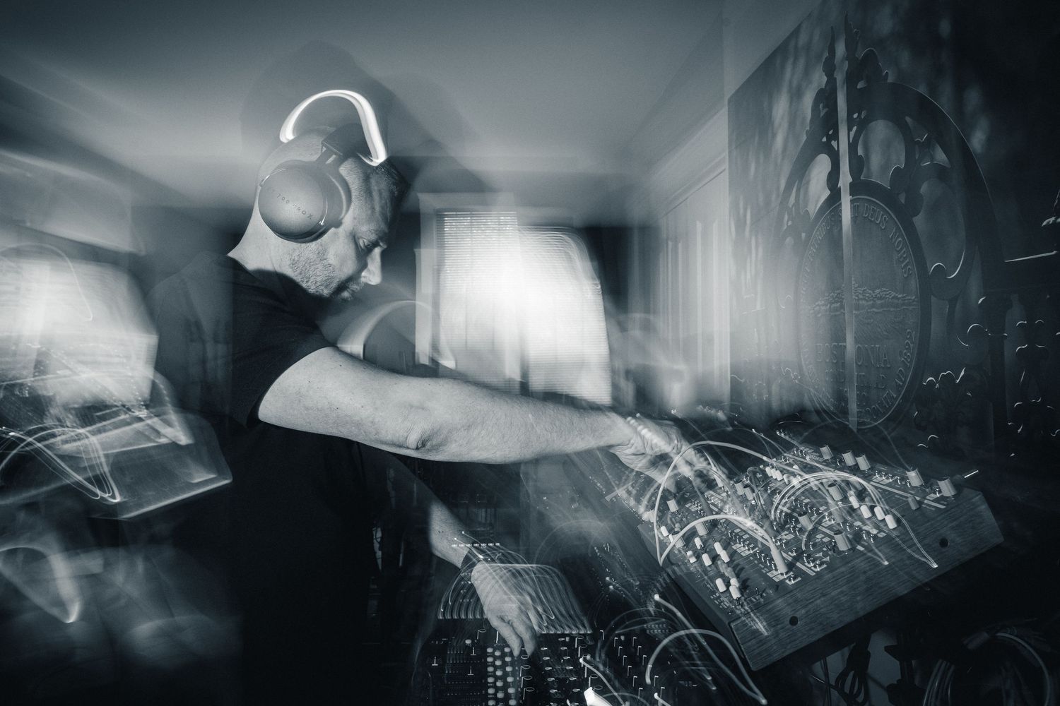 Black and white photo of a DJ wearing headphones mixing music on a modular synthesizer setup.
