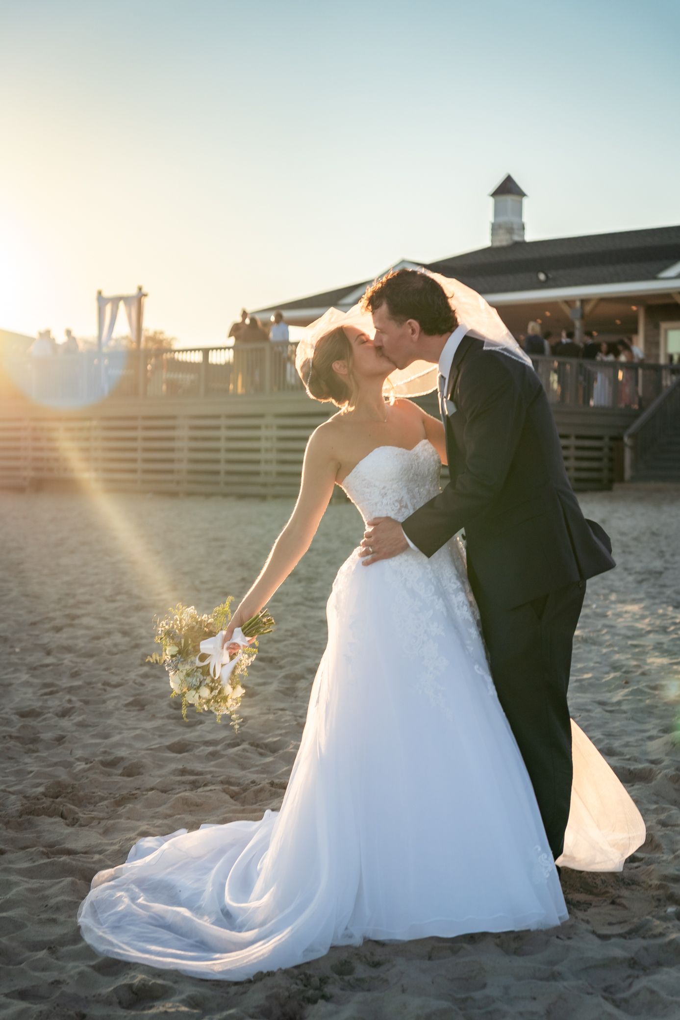 Romantic sunset beach wedding photos show couple in white dress and dark suit dipping in the sand.