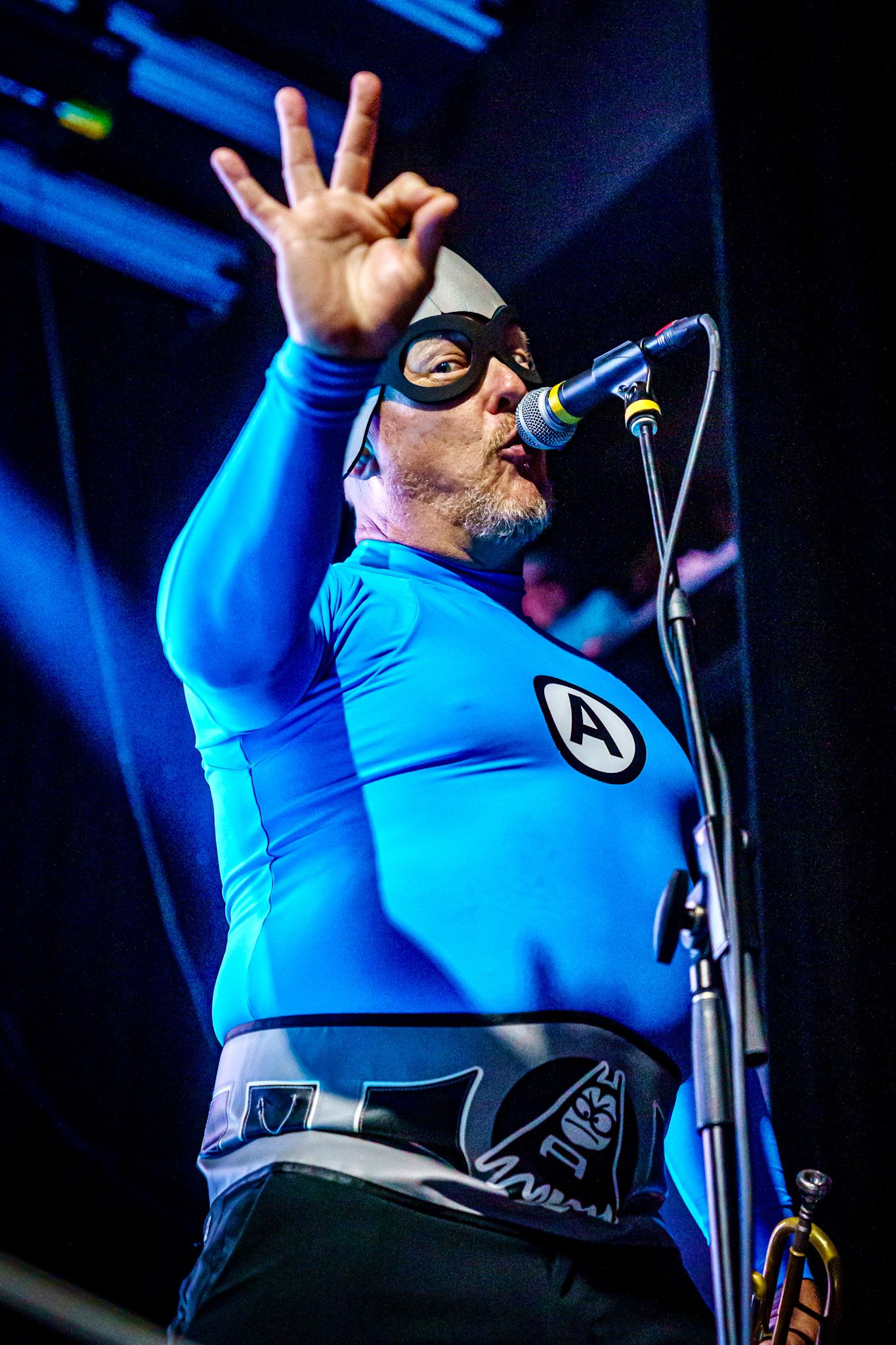 Performer in bright blue shirt singing and gesturing expressively on stage under blue lighting during a concert performance.