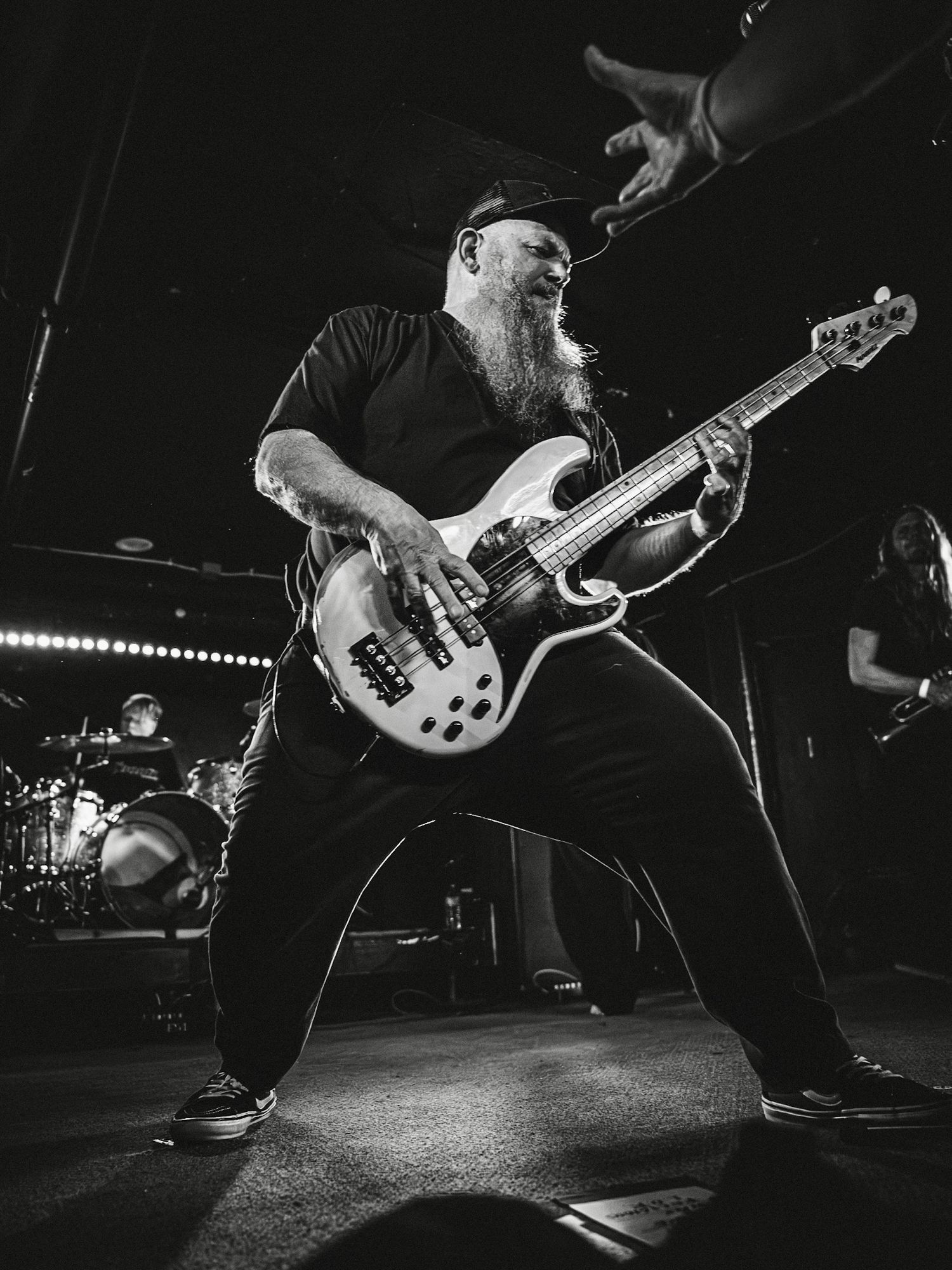Monochromatic photo of a bearded bassist (Against All Authority) performing energetically on stage with an electric bass at a live concert.