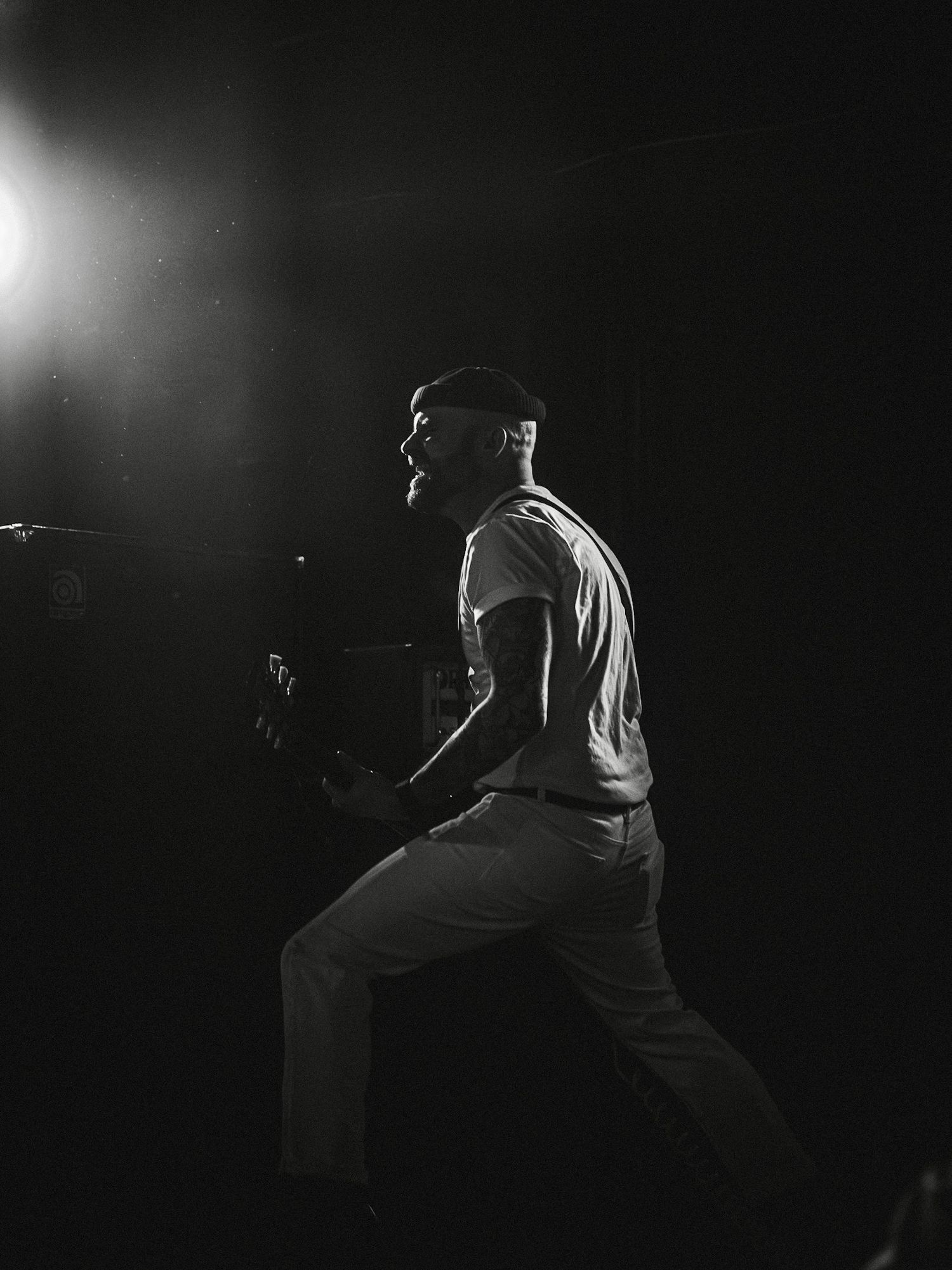 Black and white photo of a musician on stage under a dramatic spotlight, singing passionately with dynamic pose. (Band: Hell Beach)