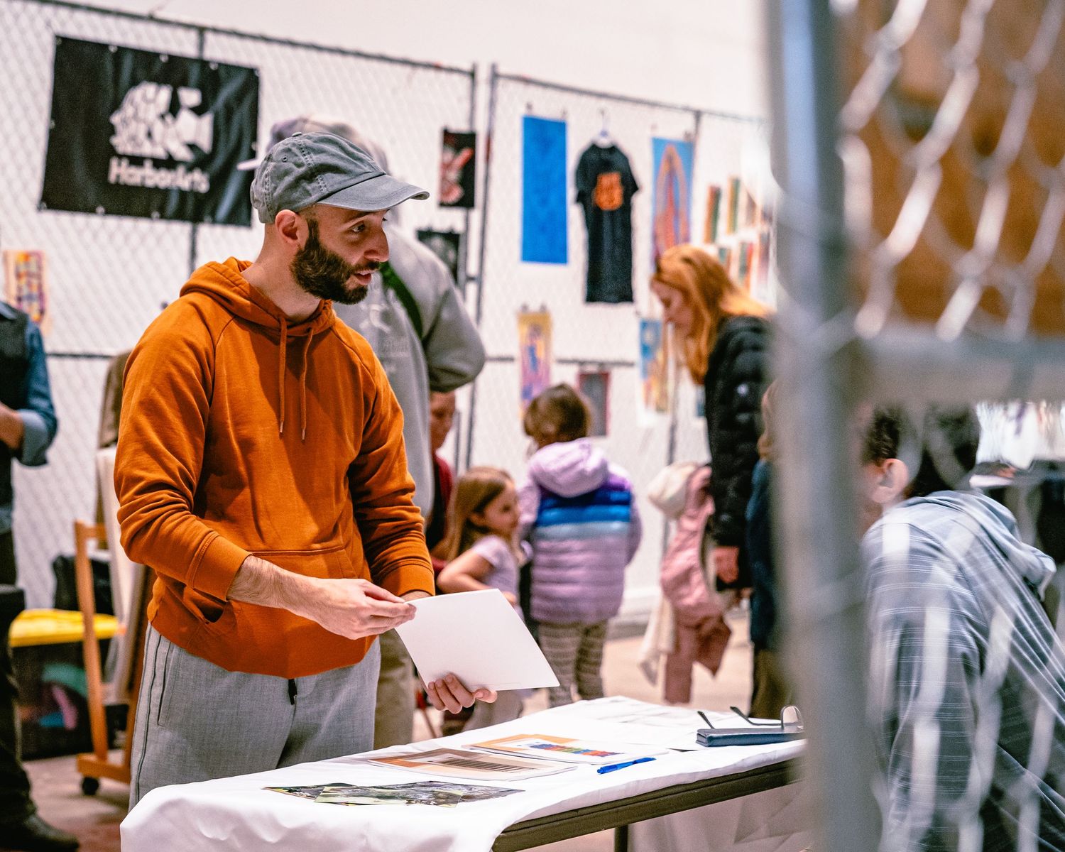 Man in orange hoodie browsing art prints at an indoor market and art fair exhibition booth, held at the ICA Watershed in East Boston.
