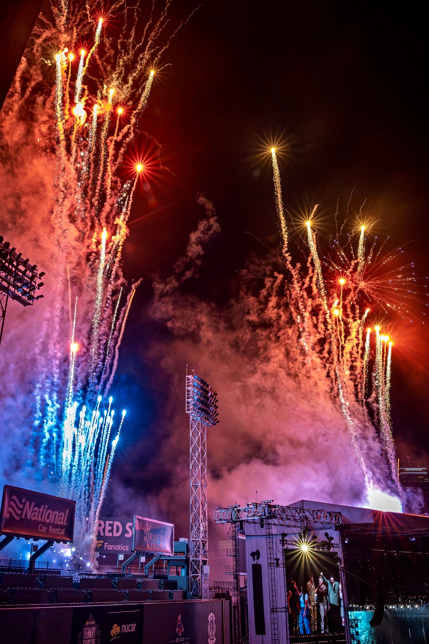 Colorful fireworks illuminate the night sky above a baseball stadium with red and blue pyrotechnics bursting dramatically.