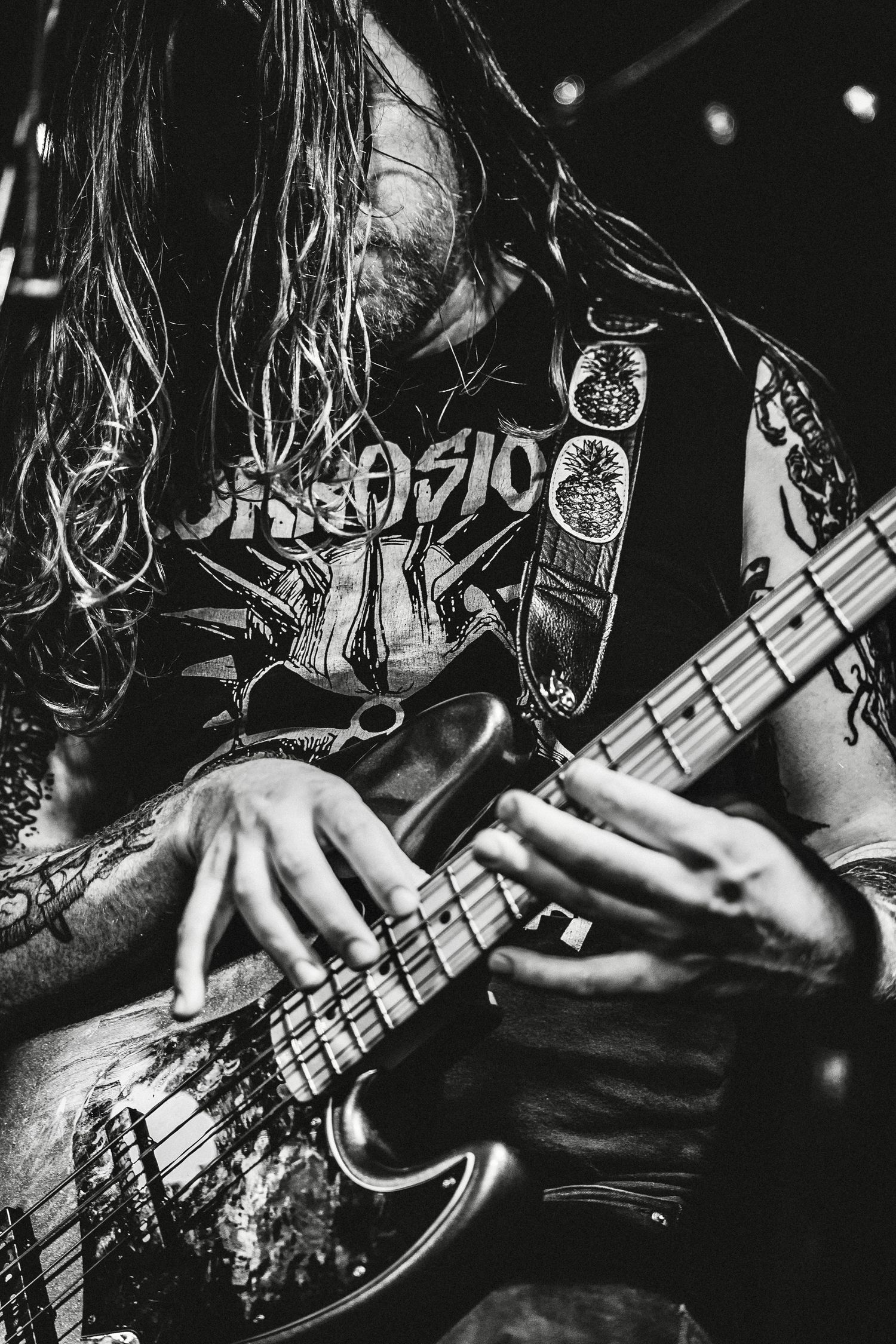 Close-up black and white shot of hands playing bass guitar during heavy metal performance.