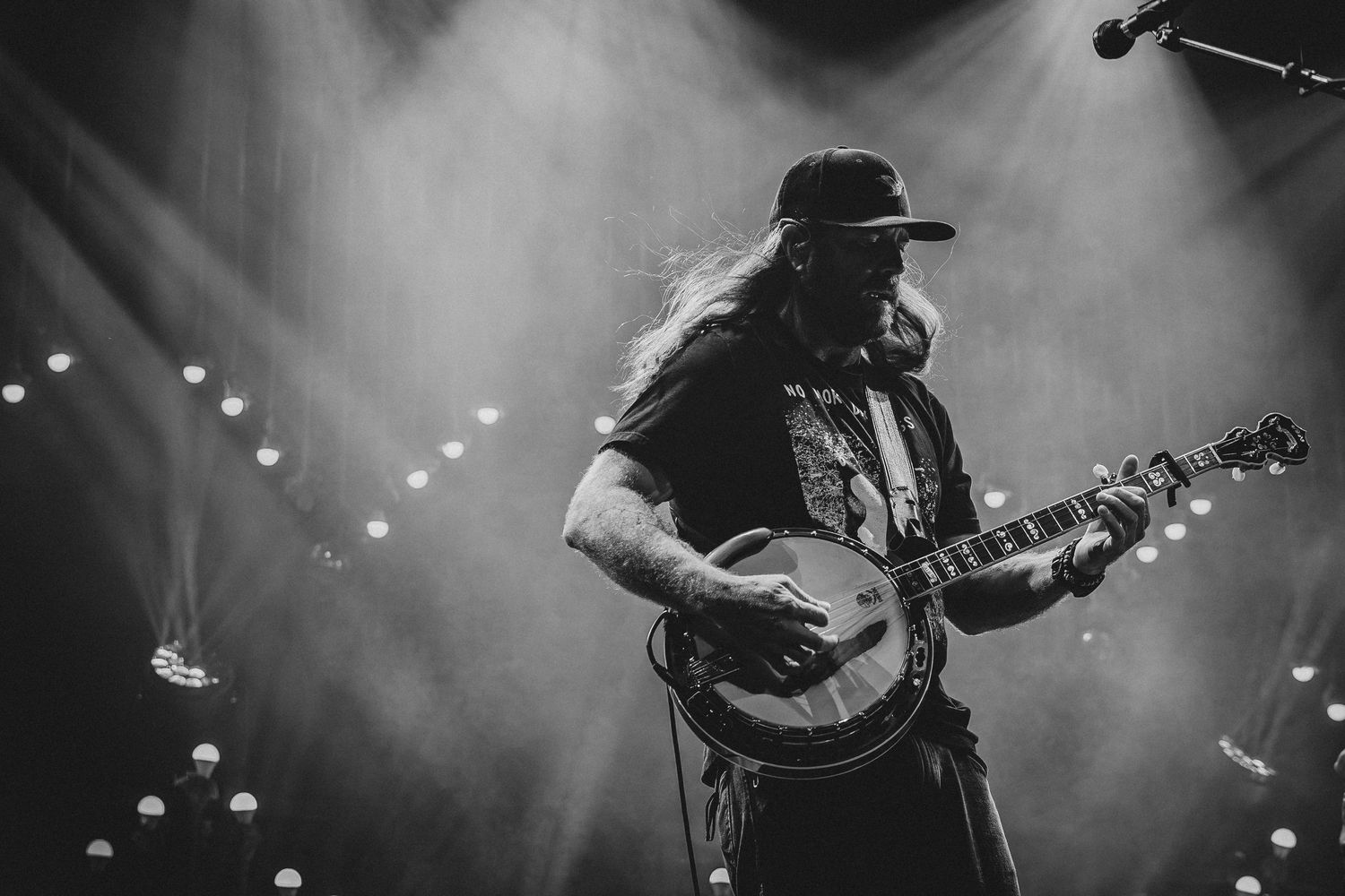 Black and white photo of a long-haired guitarist performing on stage with dramatic lighting and fog effects.
