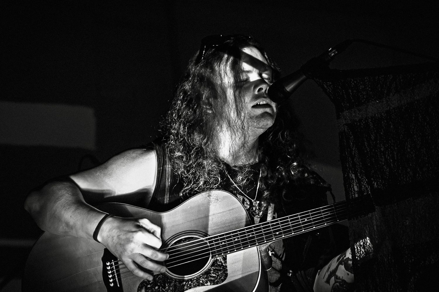 Black and white photo of a long-haired musician playing acoustic guitar on stage.