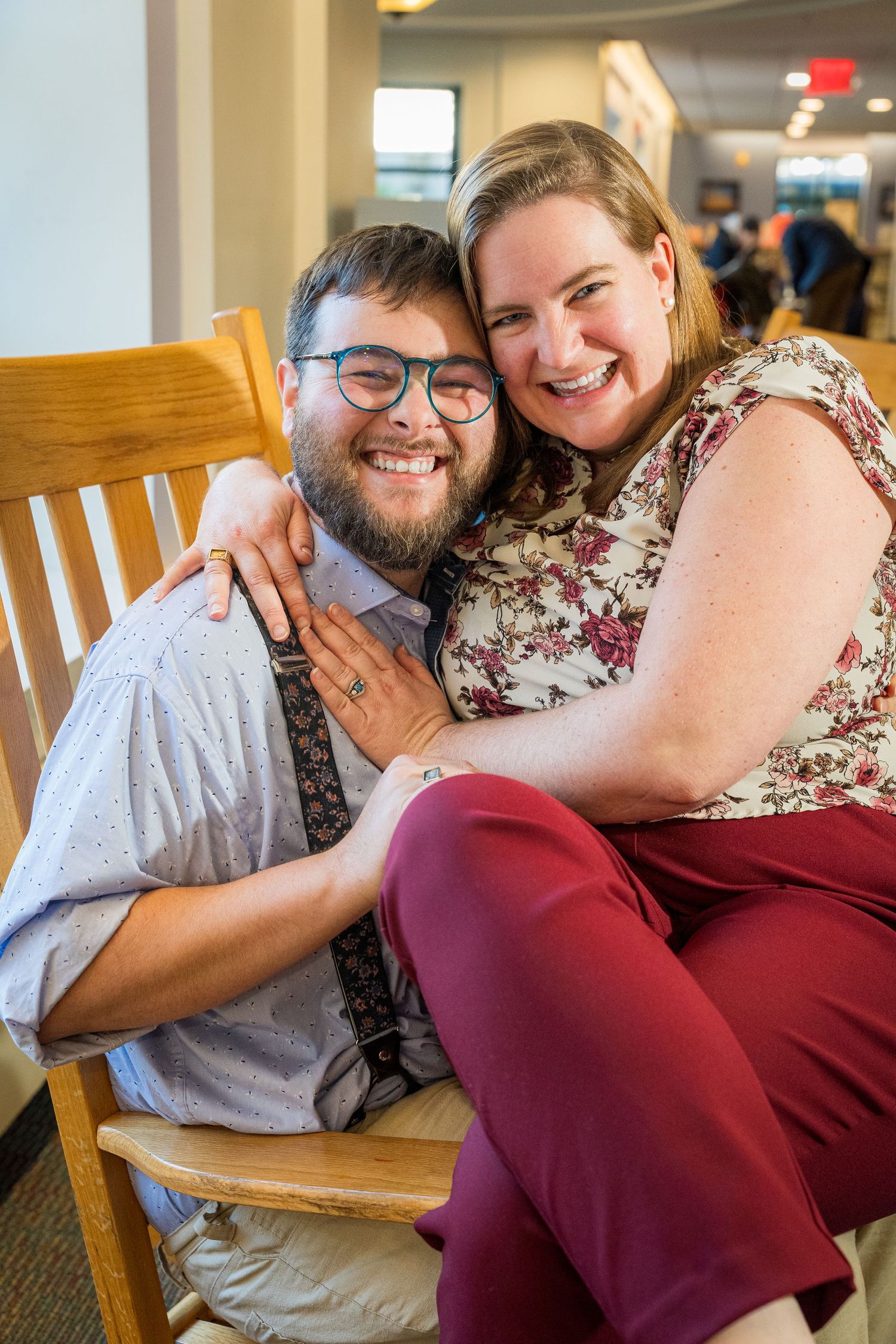 A smiling couple embraces warmly in a restaurant, woman in floral top and burgundy pants sitting on man's lap.