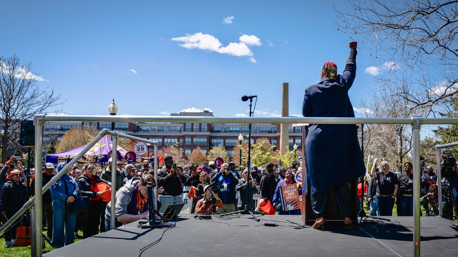 Speaker addresses diverse crowd at outdoor rally with U.S. Capitol visible in background on sunny day.