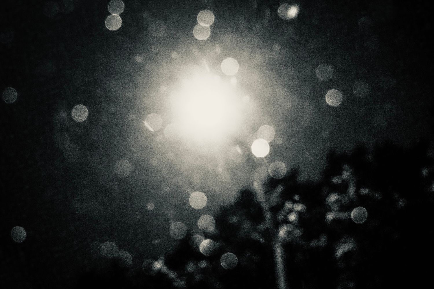 Abstract black and white bokeh photography with glowing light center and blurred circles in dark moody atmosphere.