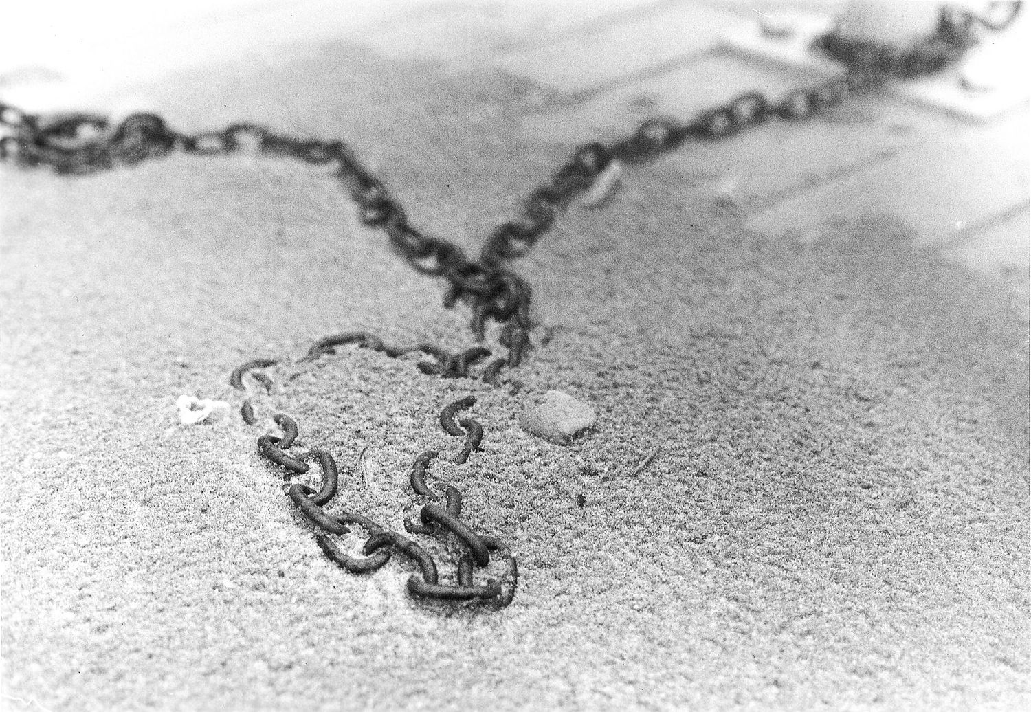 A close-up black and white photograph shows a metal chain lying on a textured surface with water droplets.